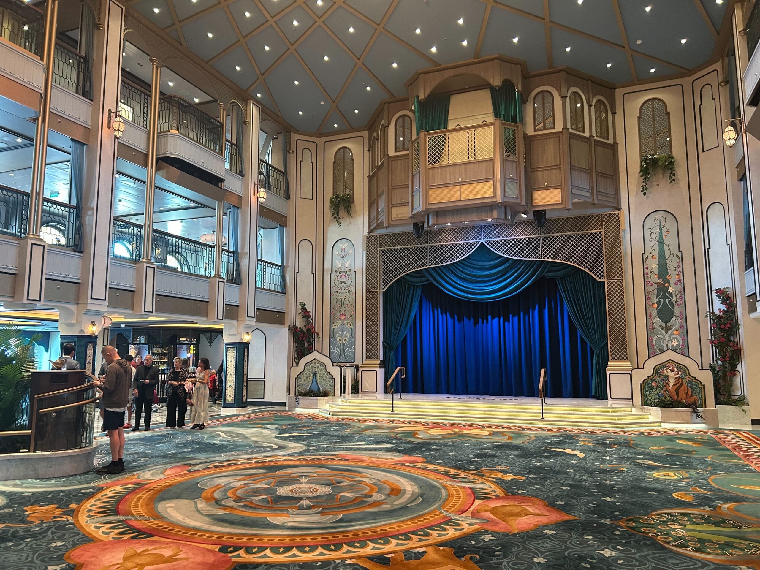 Elegant theater lobby with a blue-curtained stage, and guests gathered on Disney Cruise Line.