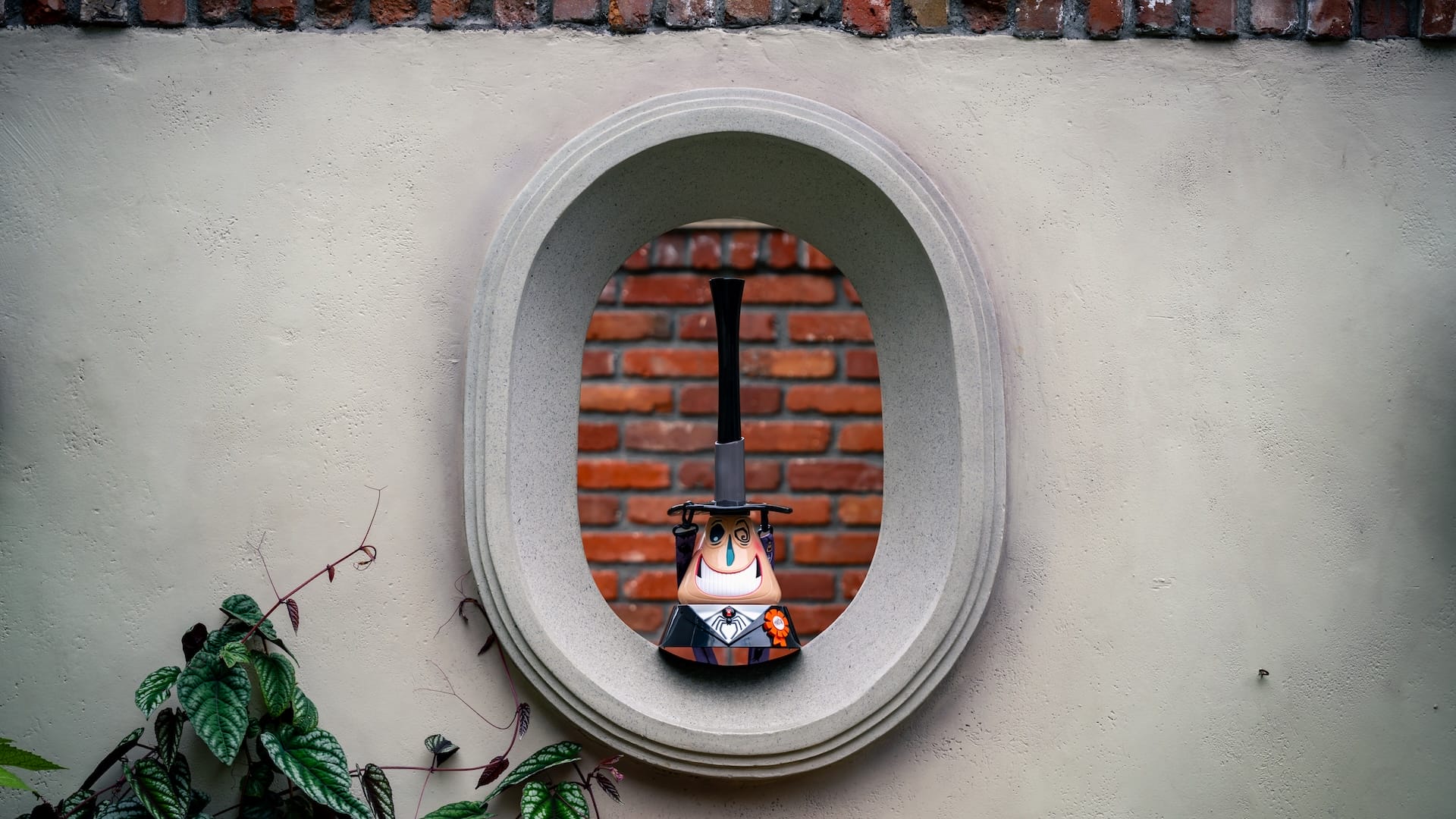 A toy witch with a tall hat peeks from a round window, echoing Halloween 2025 at the Disneyland Resort.