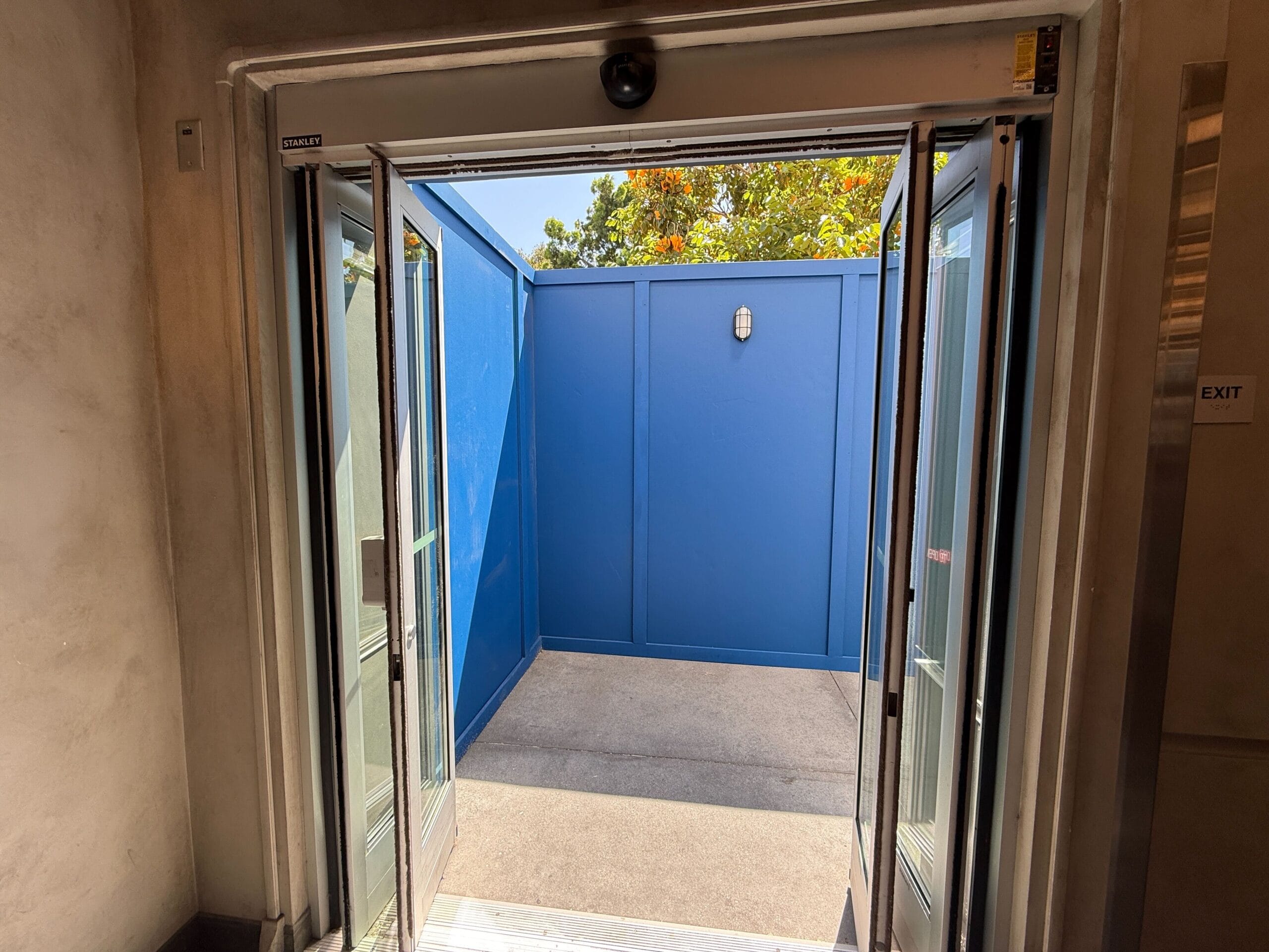 View through glass double doors opening to a small outdoor area in DCA’s Avengers Campus, enclosed by bright blue walls.