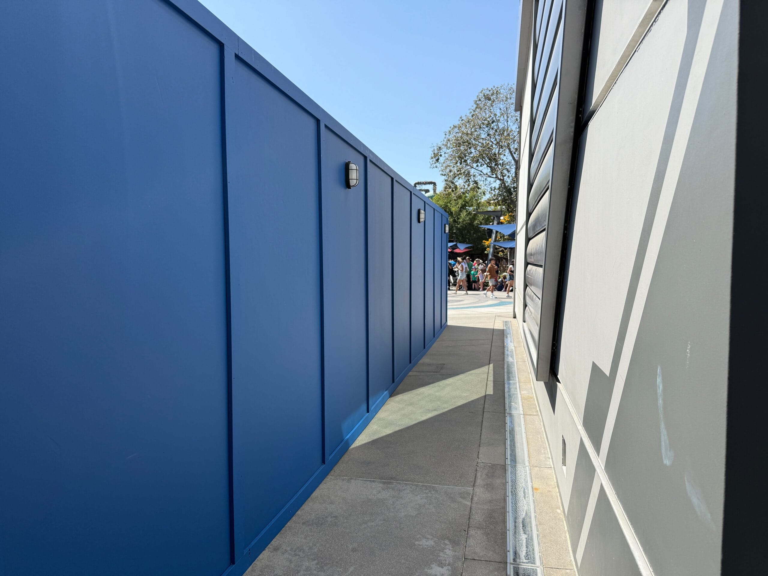 A narrow walkway between a blue construction wall and a gray building at DCA, with people visible in the distance.