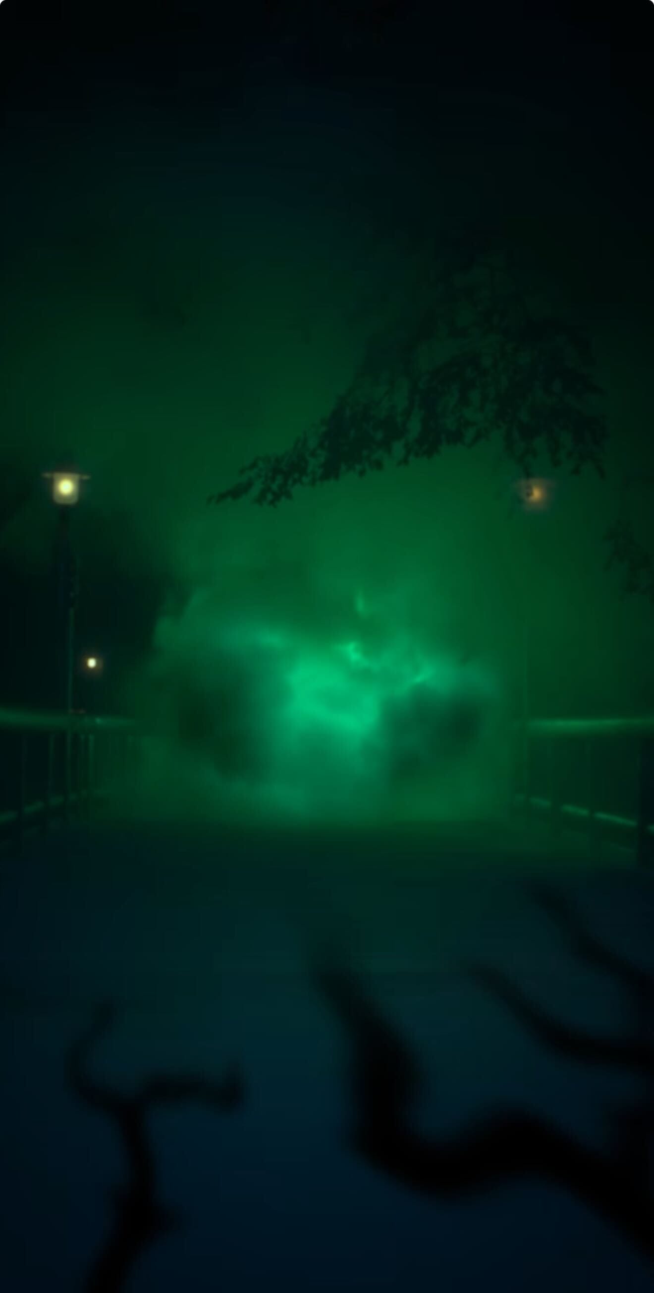 A glowing green mist, like Maleficent's magic, hovers over a dark pathway lit by distant streetlights at night.