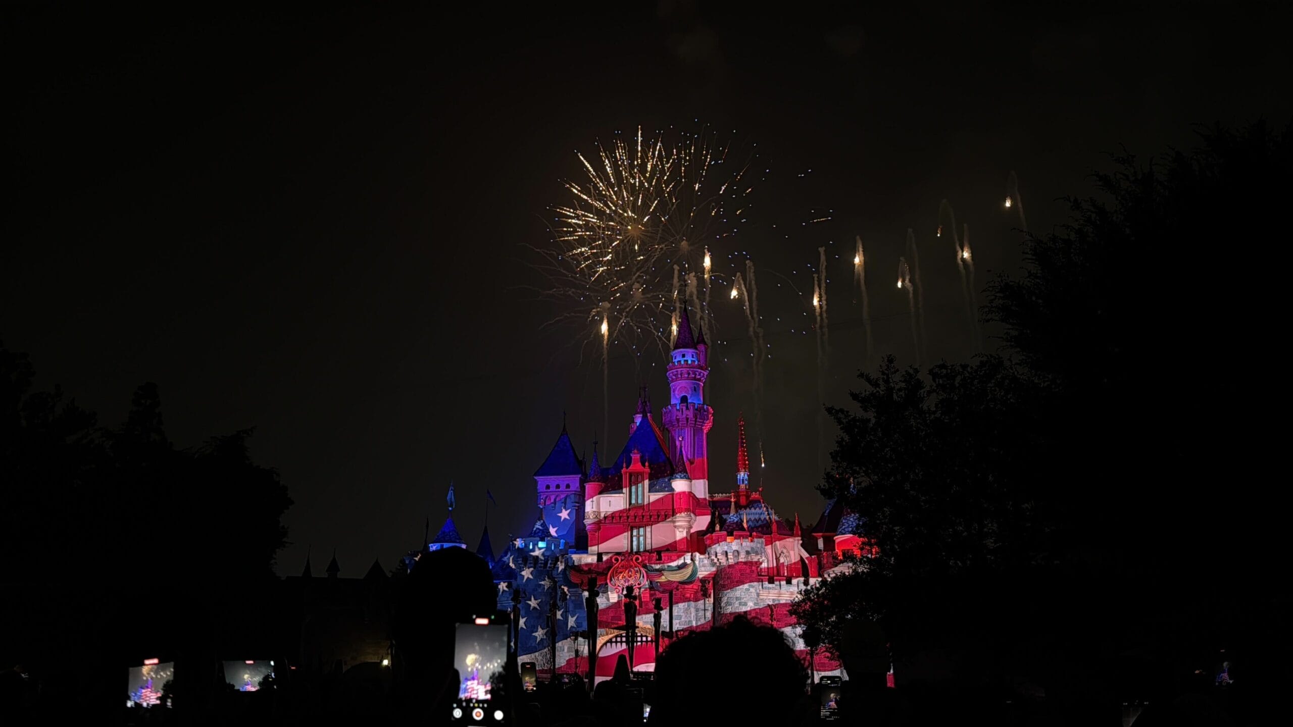 Sleeping Beauty Castle at Disneyland glows with an American flag as Celebrate America fireworks burst overhead.