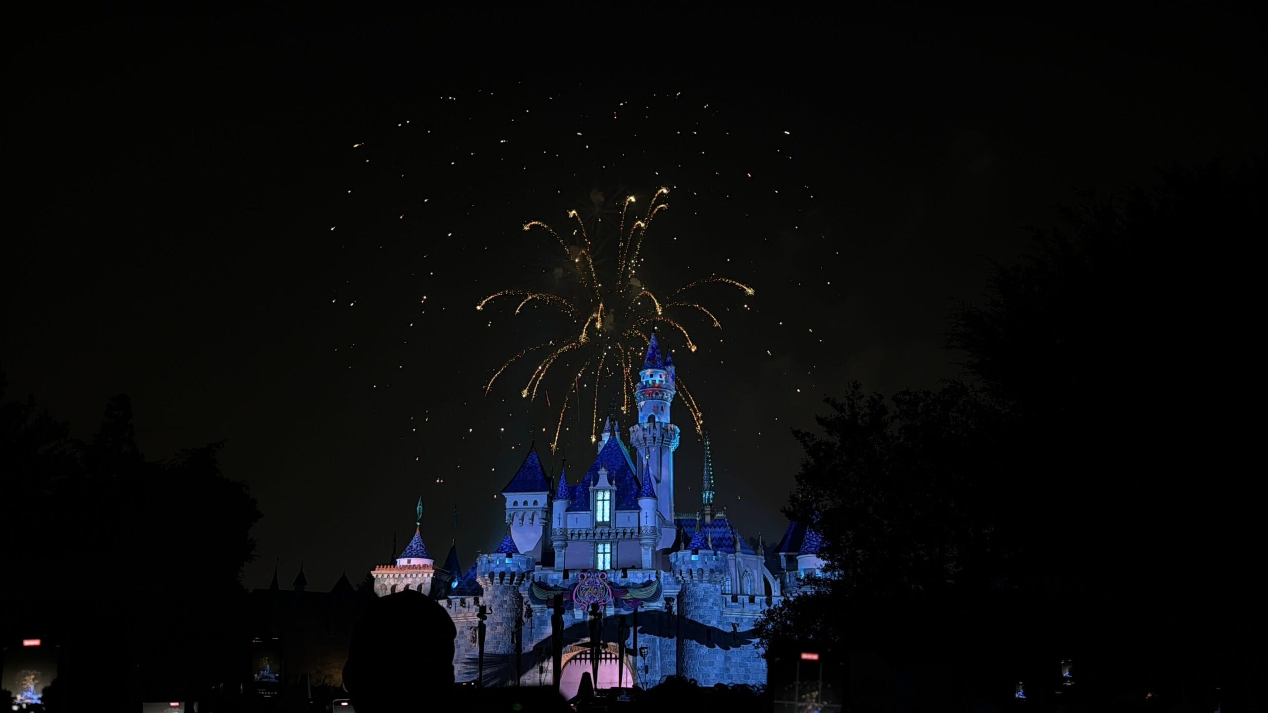 Disneyland castle illuminated at night with Celebrate America fireworks lighting up the Fourth of July sky above it.