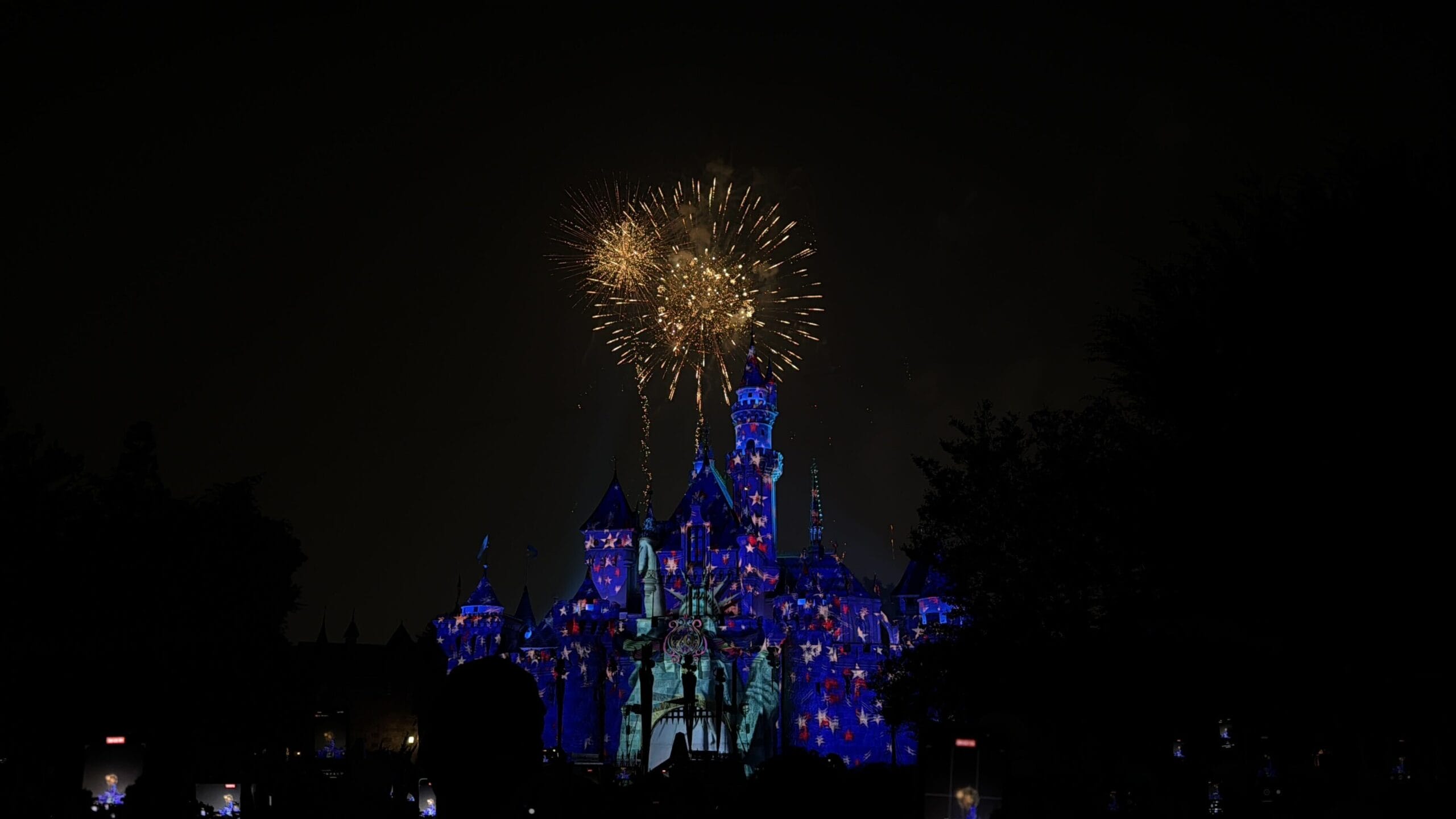 Disneyland castle illuminated at night as Celebrate America fireworks light up the Fourth of July sky above it.