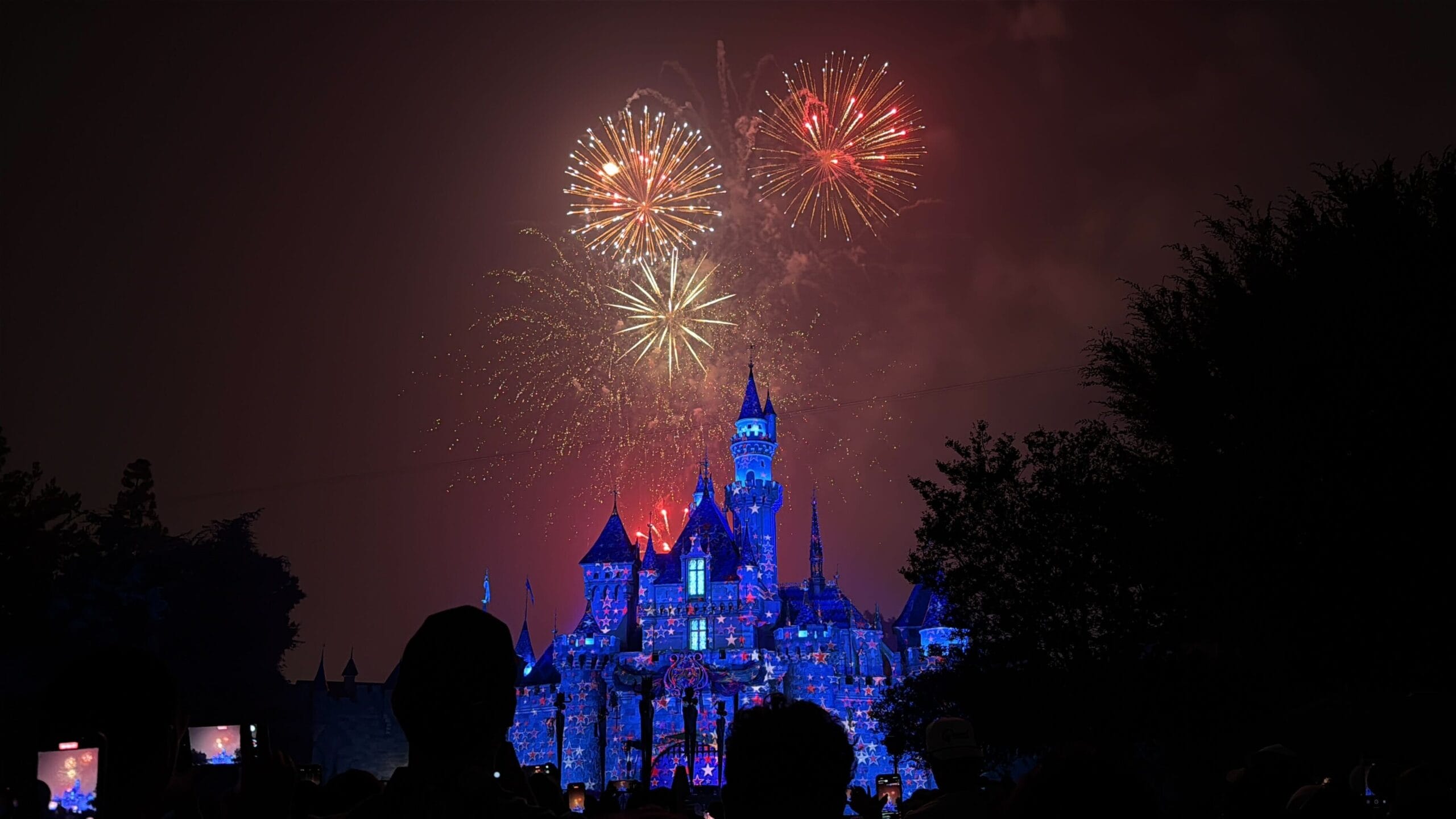 Colorful fireworks celebrate America above a brightly illuminated Disneyland castle, delighting the Fourth of July crowd below.