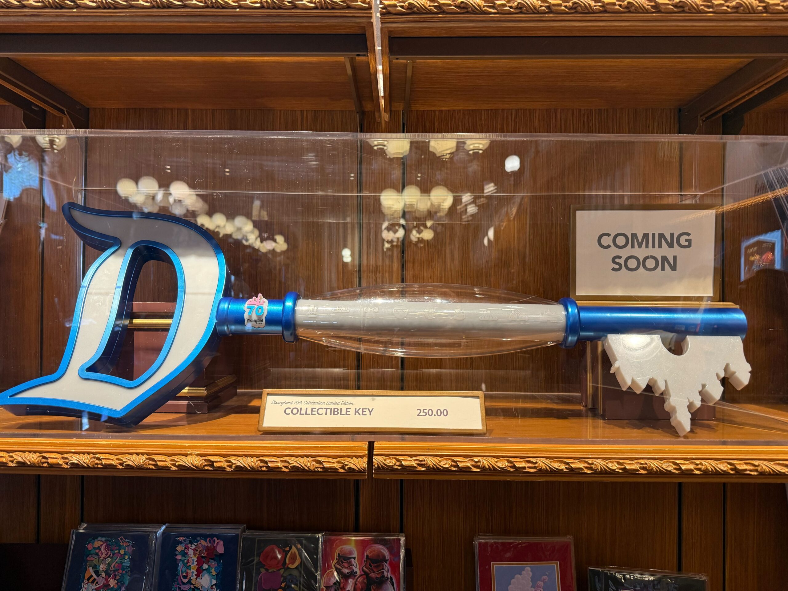 A large blue and silver Disneyland 70th Collectible Key, shaped like a "D," sits on a wooden shelf with a $250 price tag.