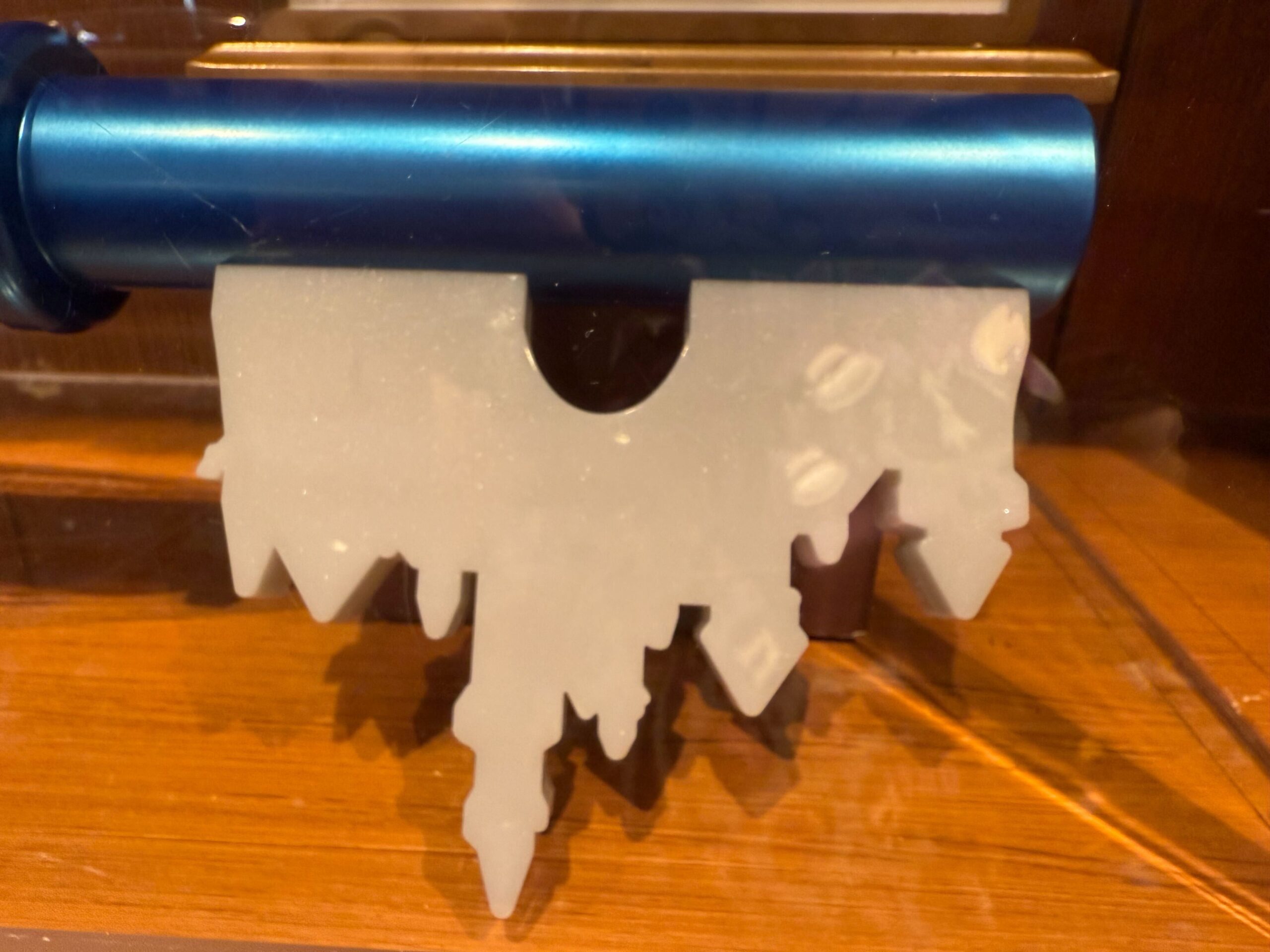 A jagged, white, icicle-shaped Disneyland collectible key hangs below a metallic blue cylinder on a wooden surface.
