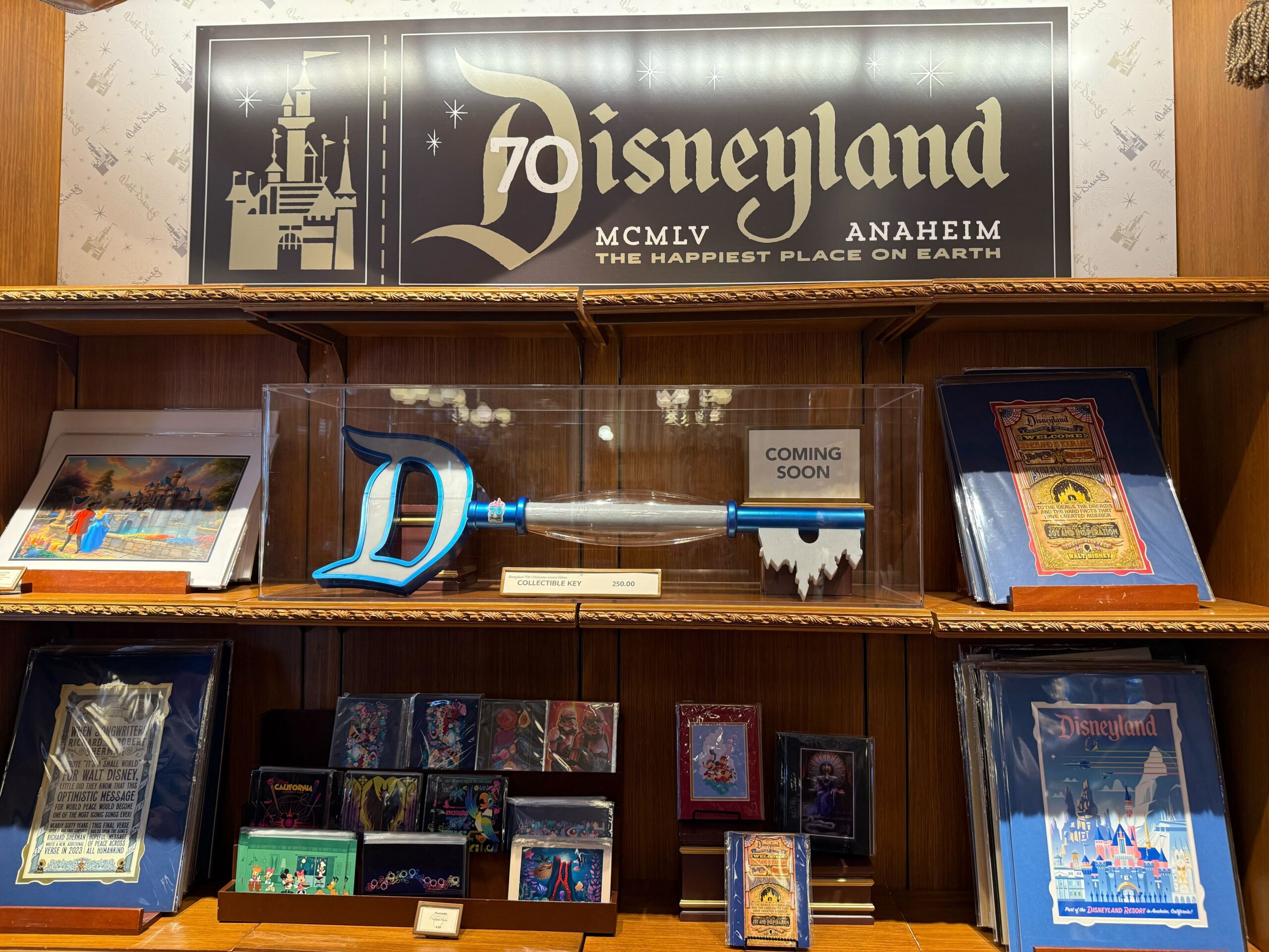Disneyland 70th Collectible Key and framed artwork displayed on wooden shelves celebrate this milestone anniversary.