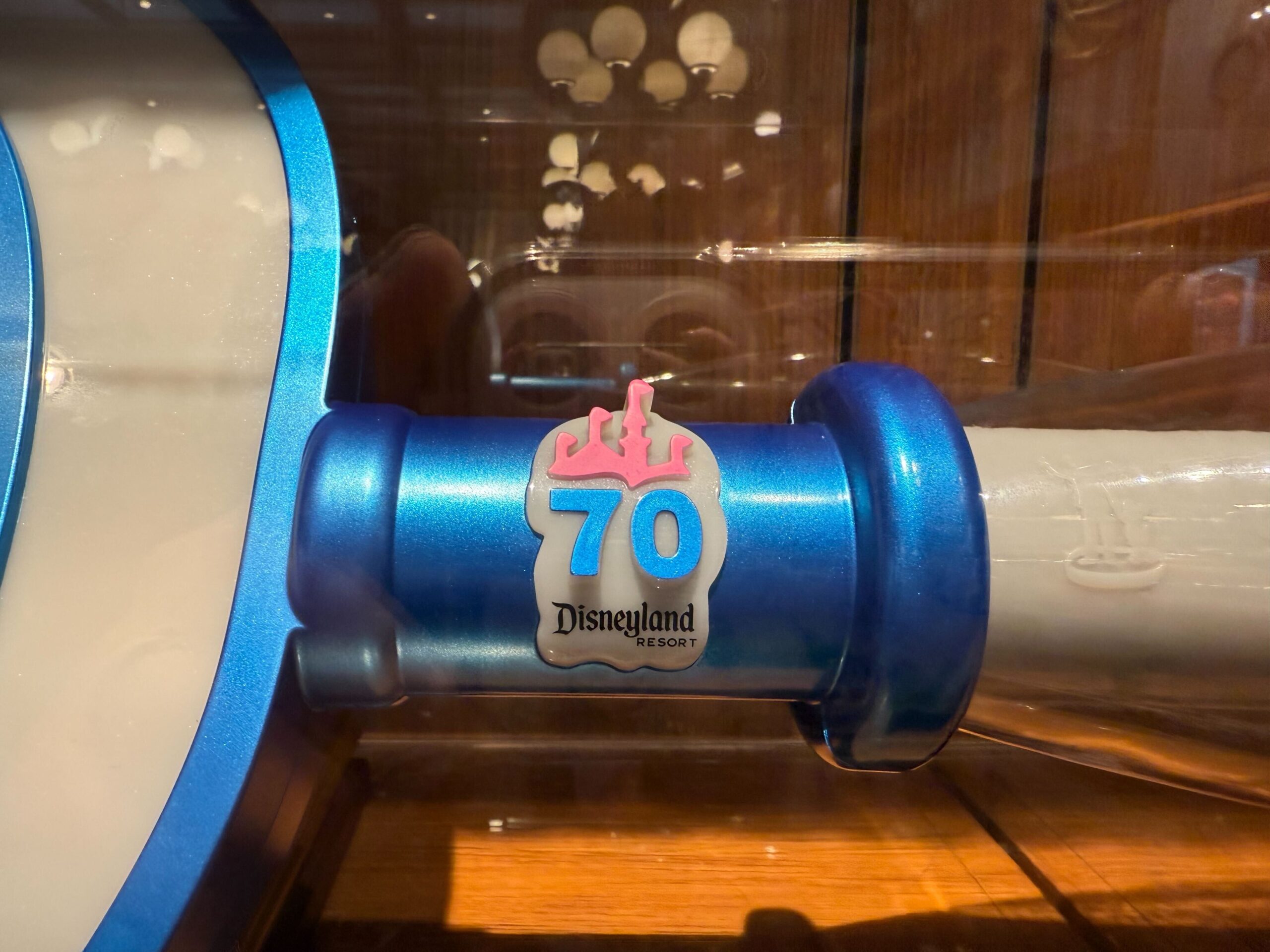 Close-up of a blue Collectible Key with the “70 Disneyland Resort” logo and pink castle, reflecting lights in the background.