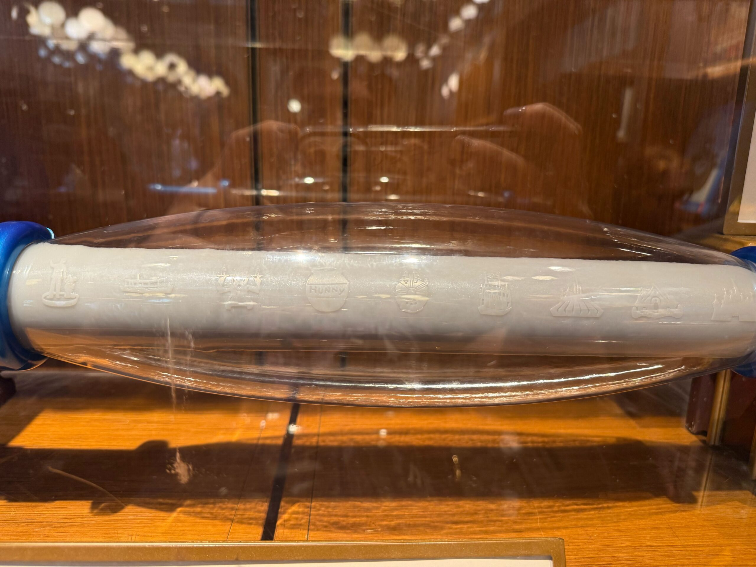 A cylindrical white Disneyland Collectible with faint engravings, displayed in a glass case on a wooden surface.
