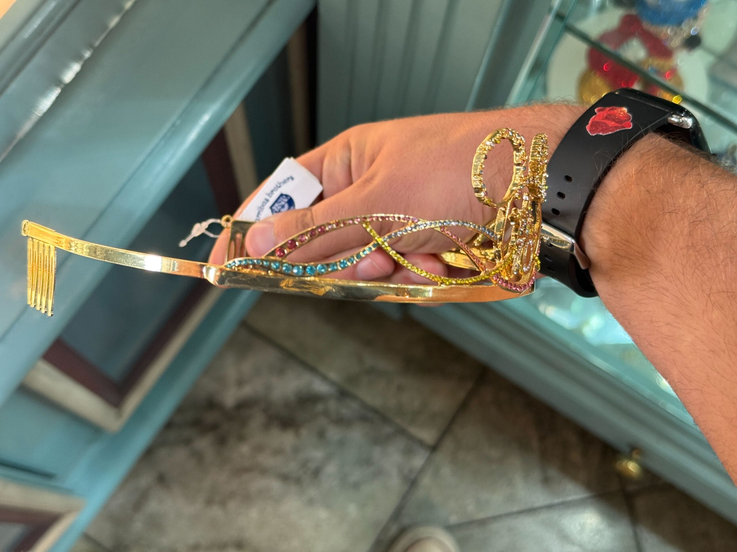 A hand holding an ornate, gold and jeweled fork with decorative swirls and blue gemstones.