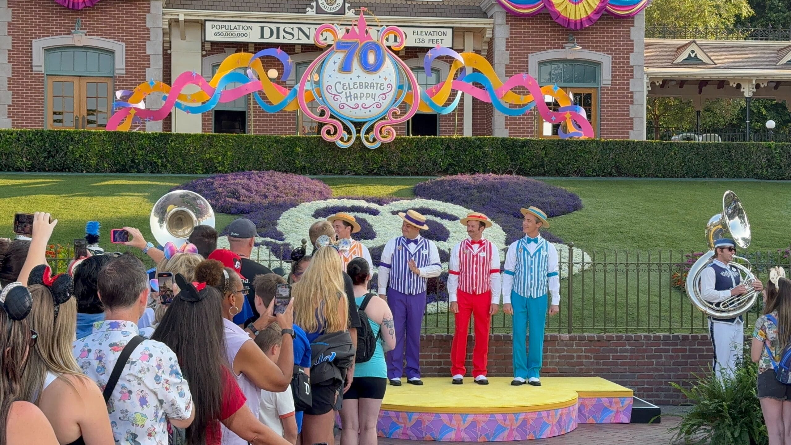 A barbershop quartet performs as people watch and take photos at the Disneyland 70th Anniversary entrance.