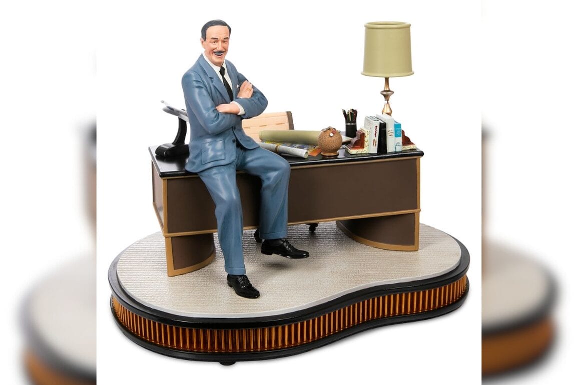 Walt Disney talking figure of a man in a blue suit sitting at a desk with office items, lamp, and books.