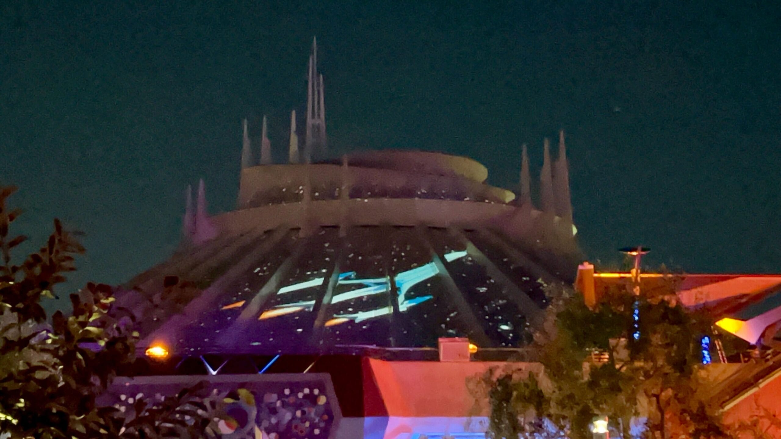 Space Mountain at night with Fantastic Four projections illuminating its domed exterior against a dark sky.