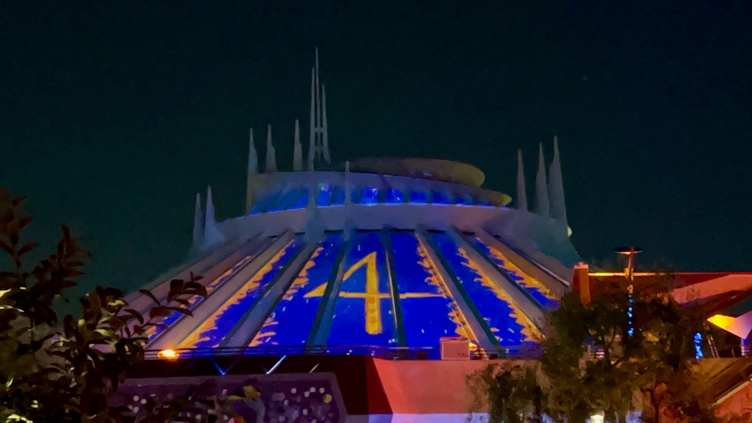 Space Mountain dome at night, glowing blue with a large yellow "4" from First Steps Projections for Fantastic Four.