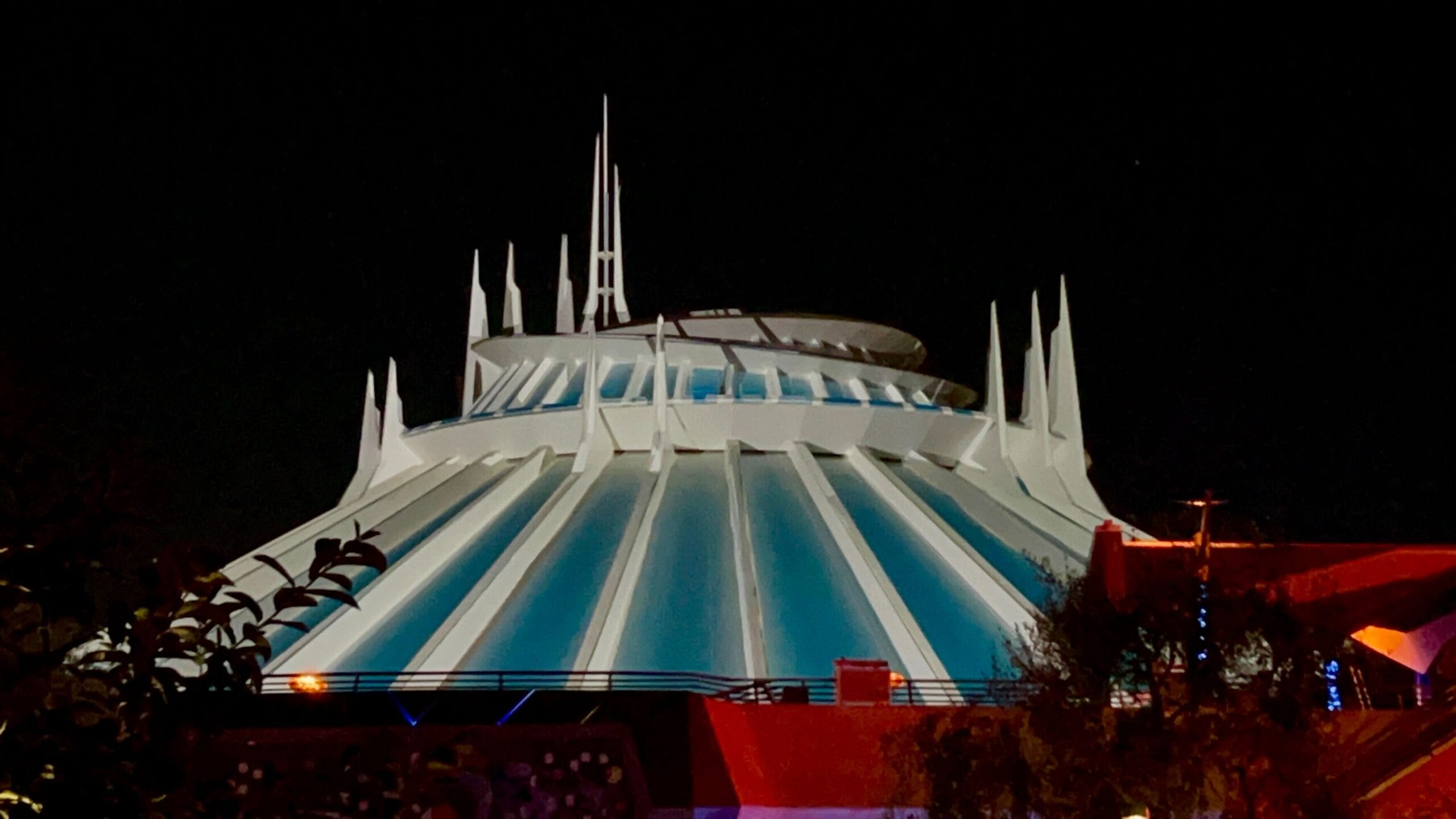 Space Mountain at night, illuminated blue and white, features First Steps Projections against the dark sky.
