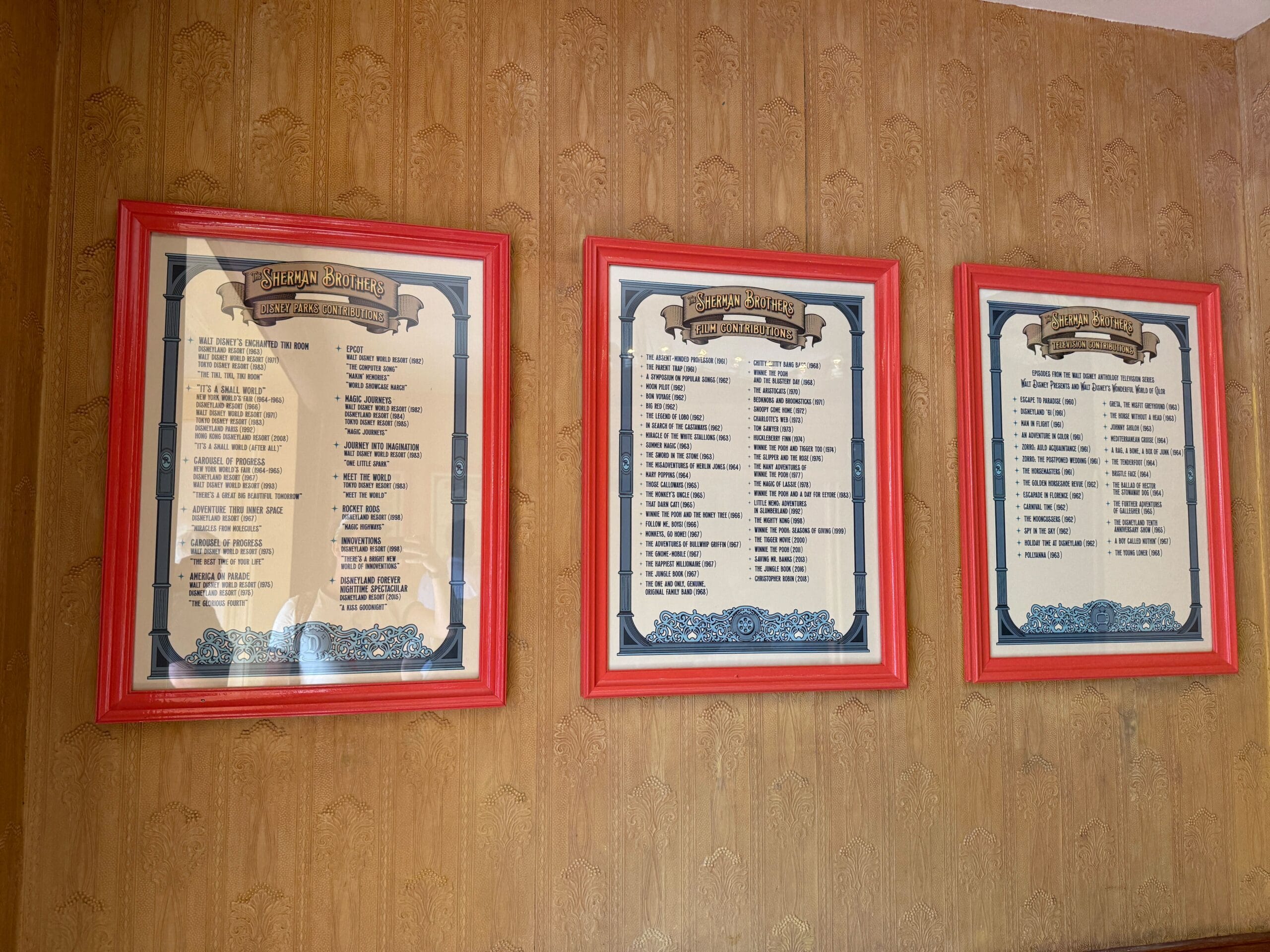 Three framed menus with red borders hang on a patterned tan wall at Main Street Cinema in Disneyland 70.