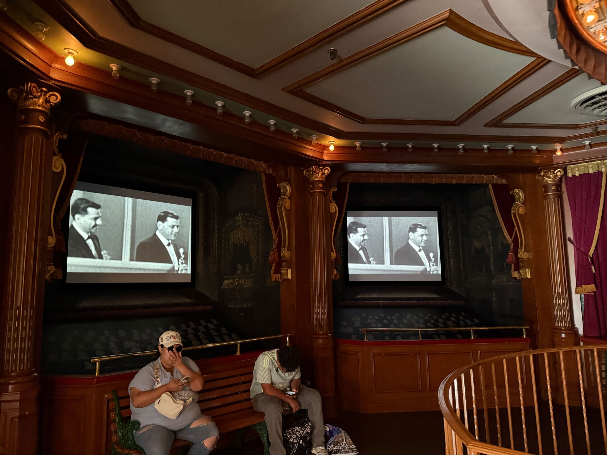 Two people sit in Main Street Cinema, watching a black and white film in a cozy Disneyland 70 tribute setting.