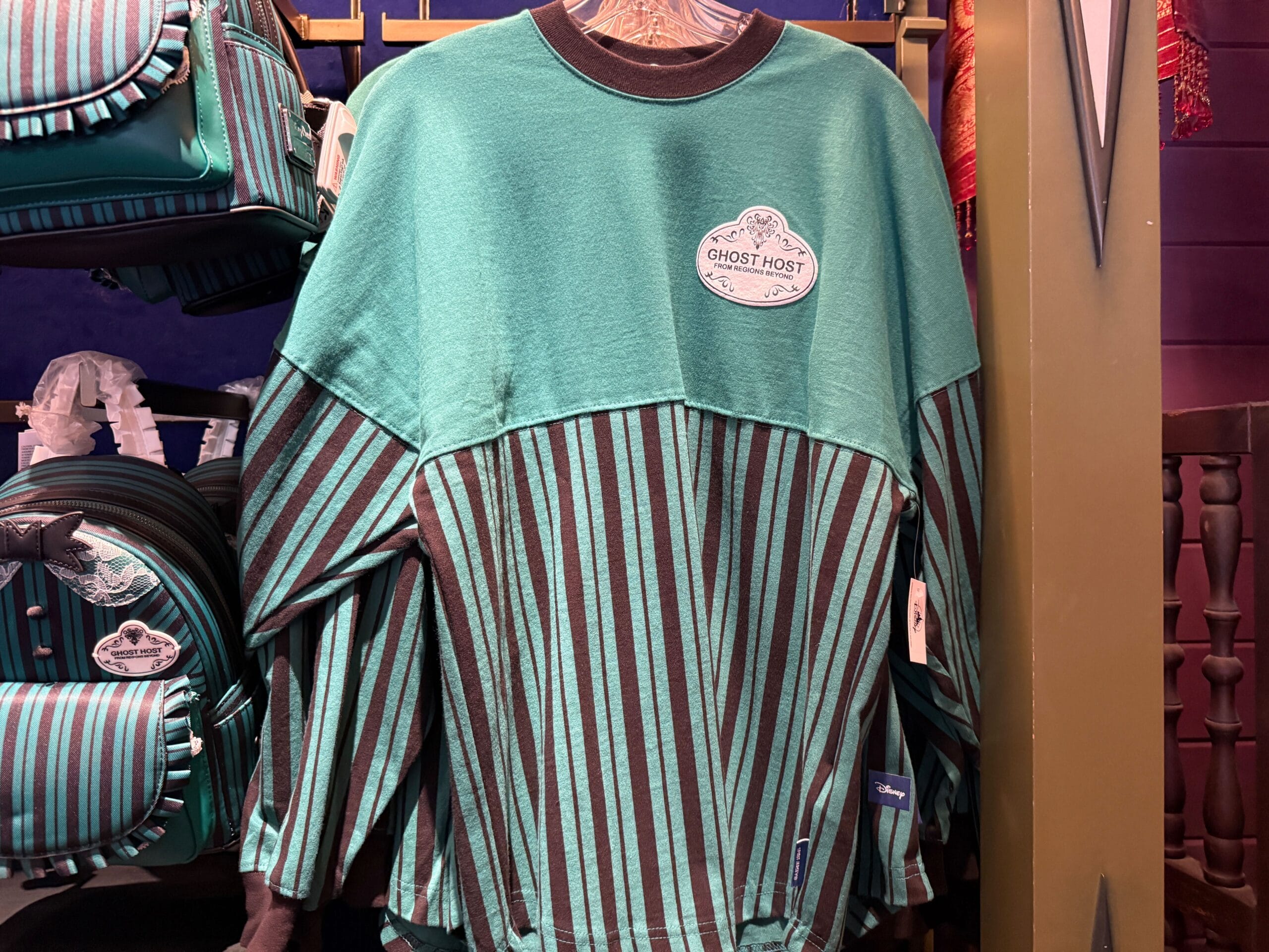 A green and black striped shirt with a "Ghost Host" badge, part of HM Merchandise at Disneyland, displayed in-store.