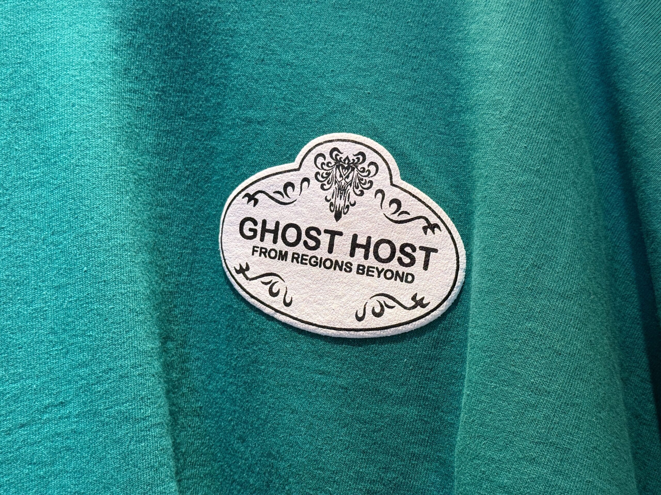 A Disneyland HM Merchandise badge reads "Ghost Host from regions beyond" on a teal fabric background.