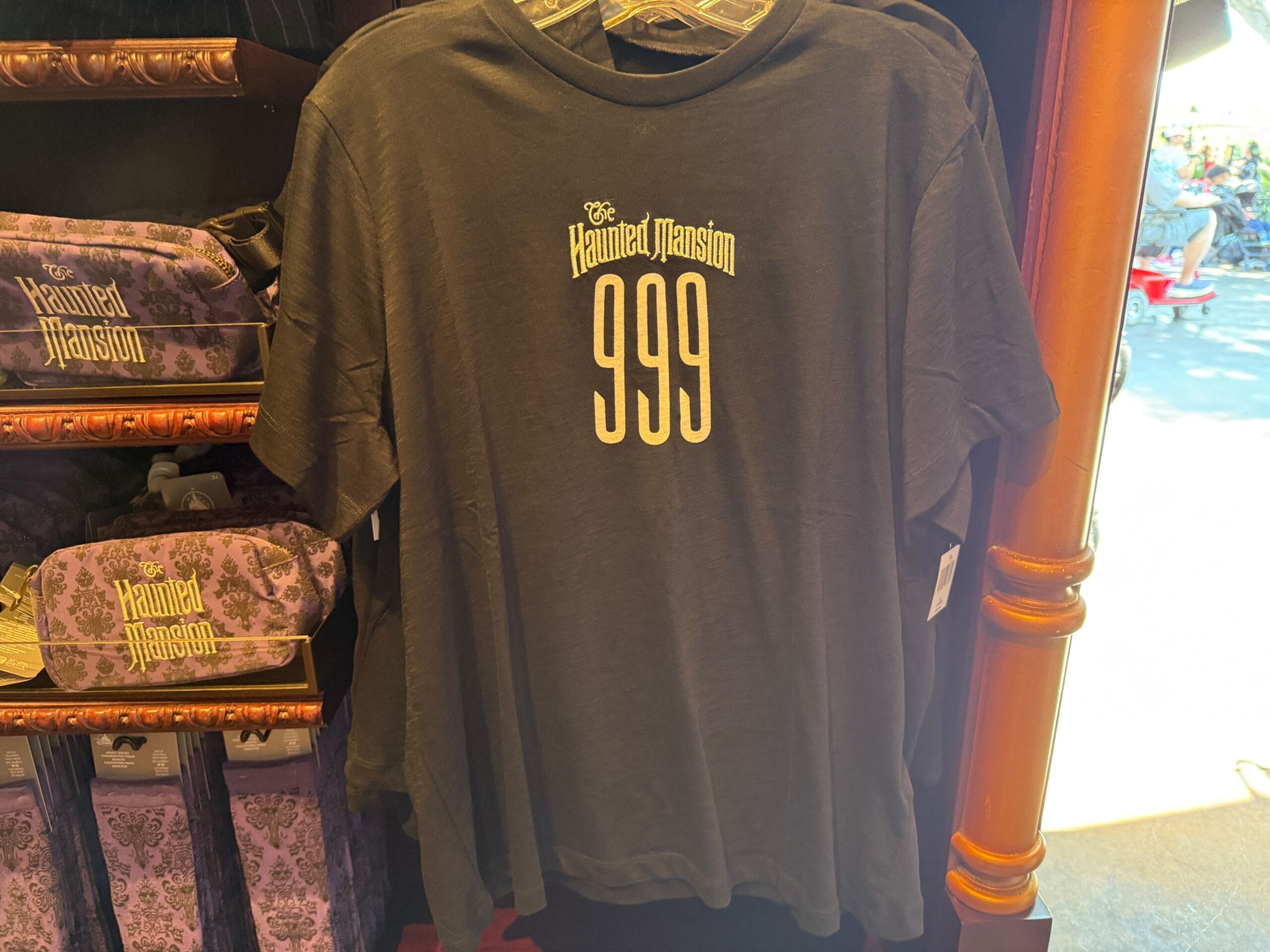 Black Haunted Mansion t-shirt with "999" on front, part of exclusive Disneyland HM Merchandise, displayed in-store.