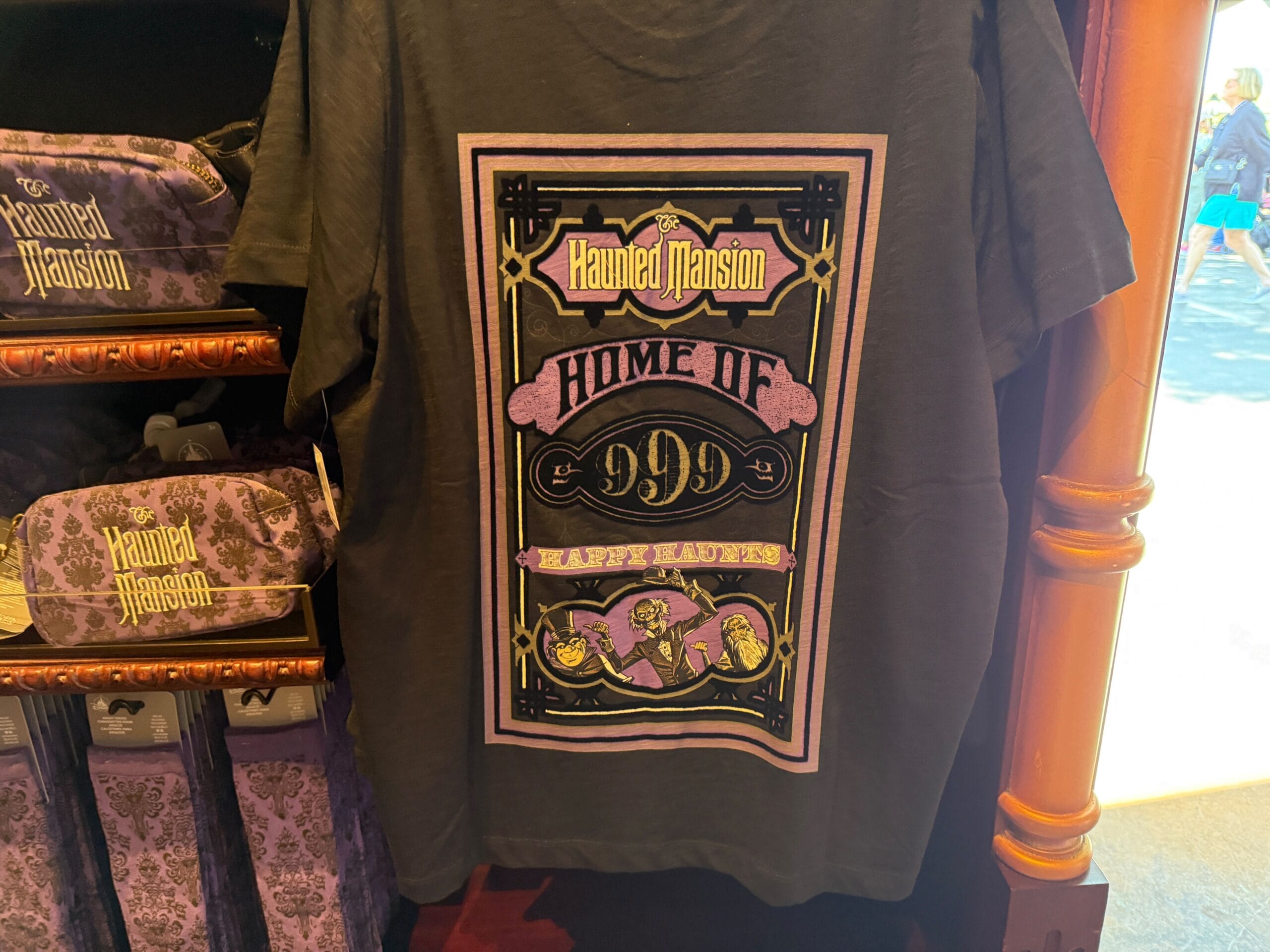Black Haunted Mansion t-shirt—Disneyland merchandise with "Home of 999 Happy Haunts" and purple, gold ghost illustrations.
