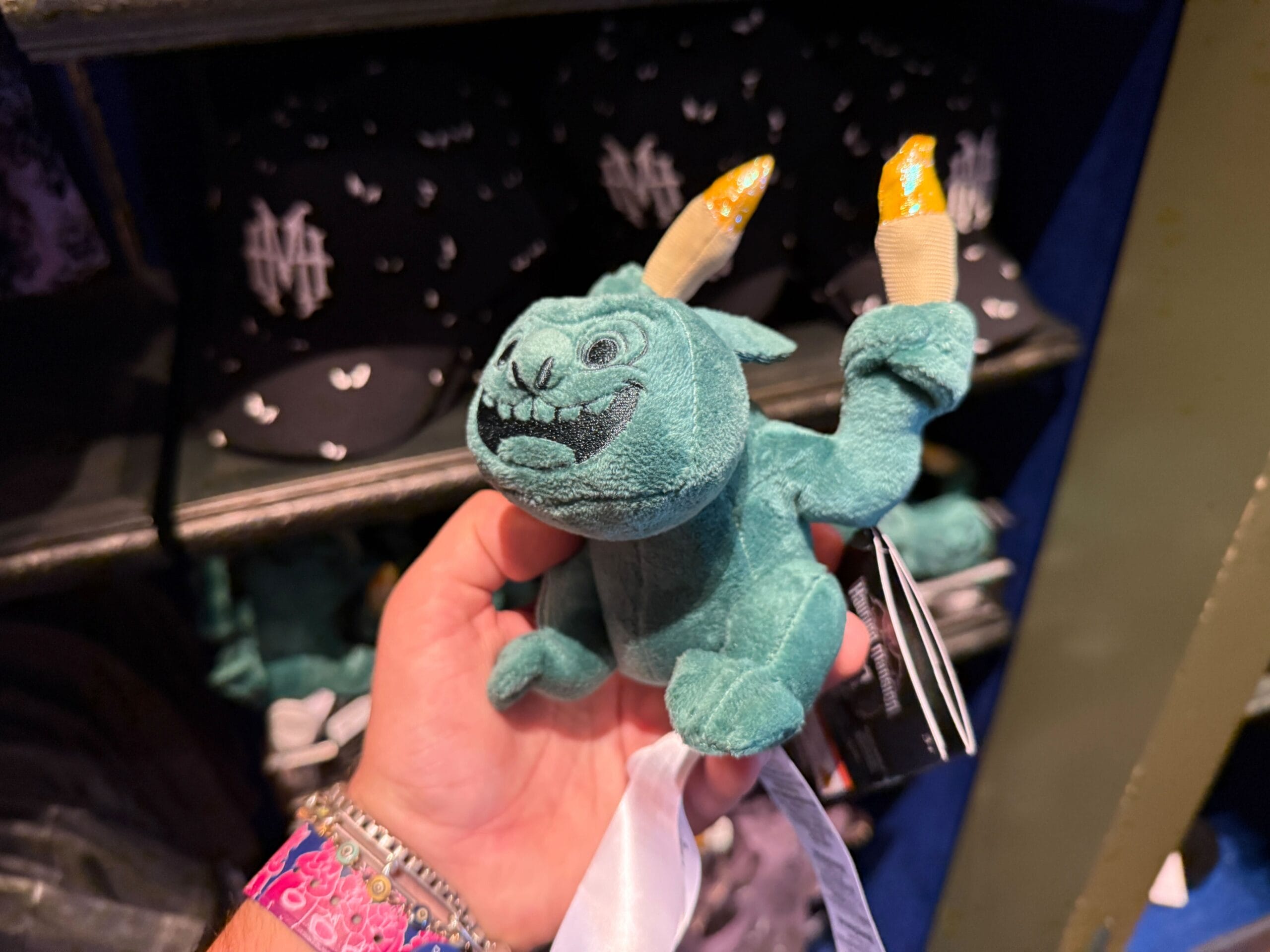 A person holds a small plush toy of a blue-green monster, exclusive to Disneyland's HM Merchandise collection.