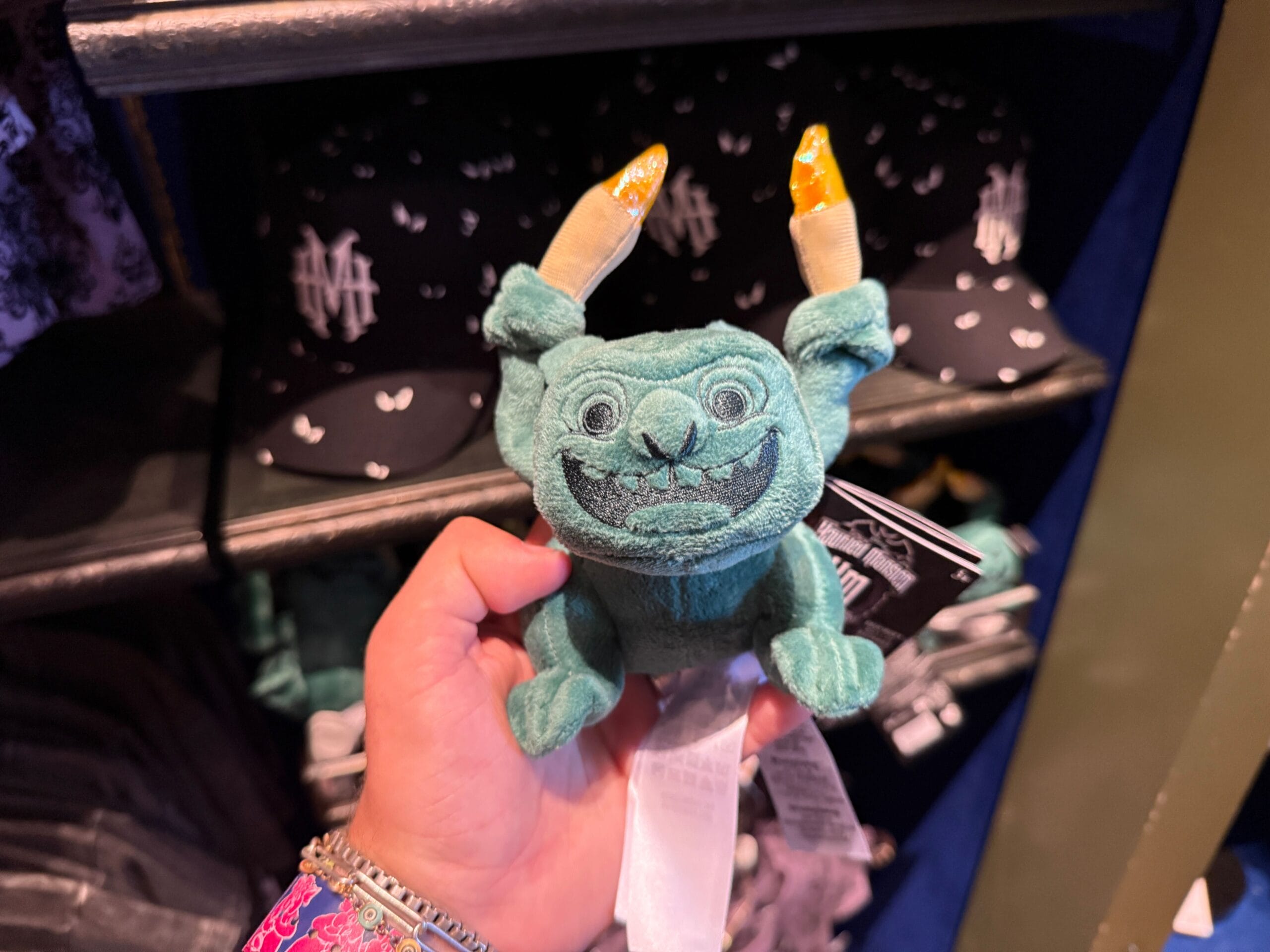 A hand holds a small, green plush toy—part of the whimsical Disneyland merchandise collection.