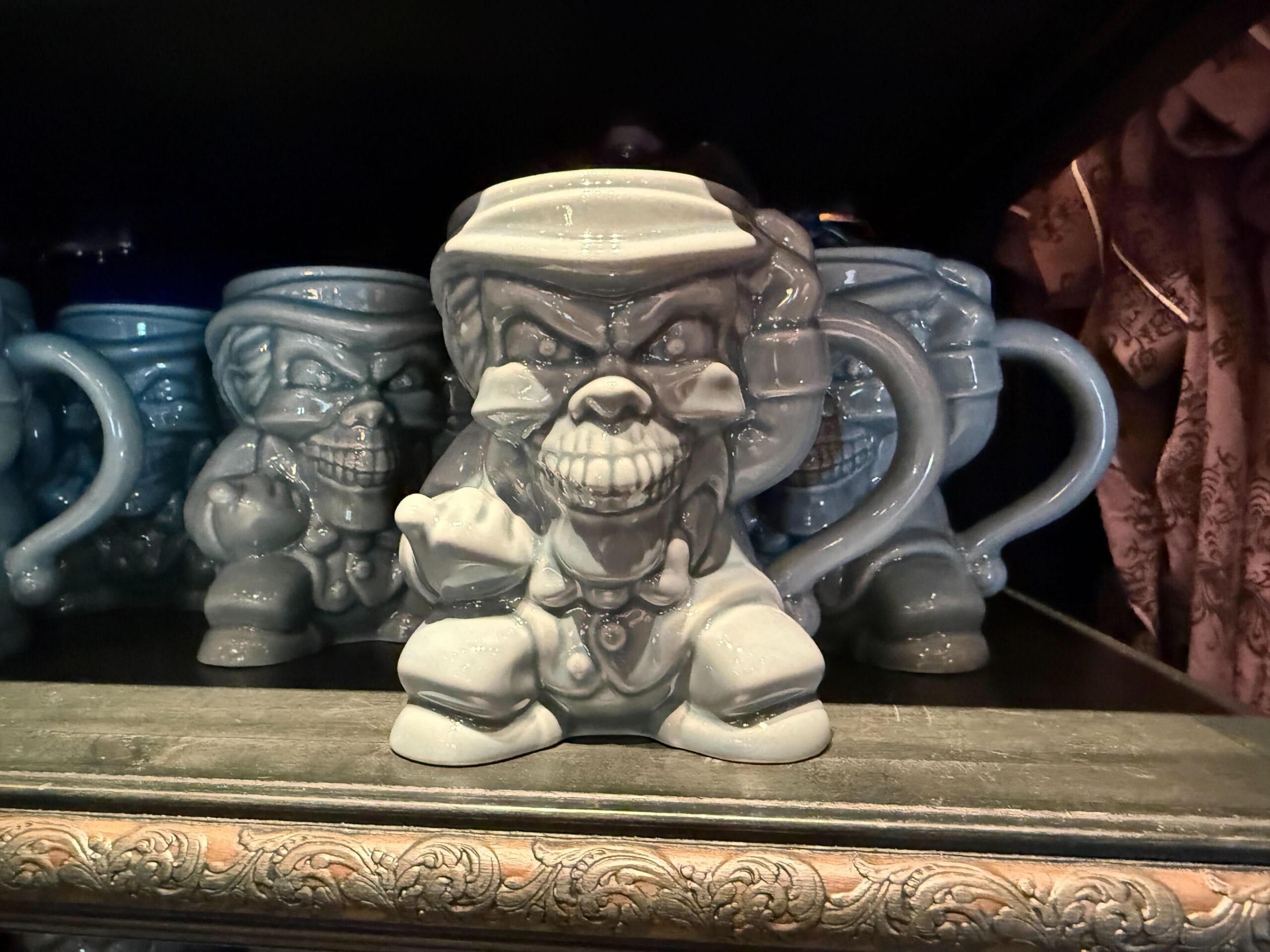 Gray mugs shaped like angry cartoon clowns with clenched fists, reminiscent of Disneyland HM Merchandise, displayed on a shelf.