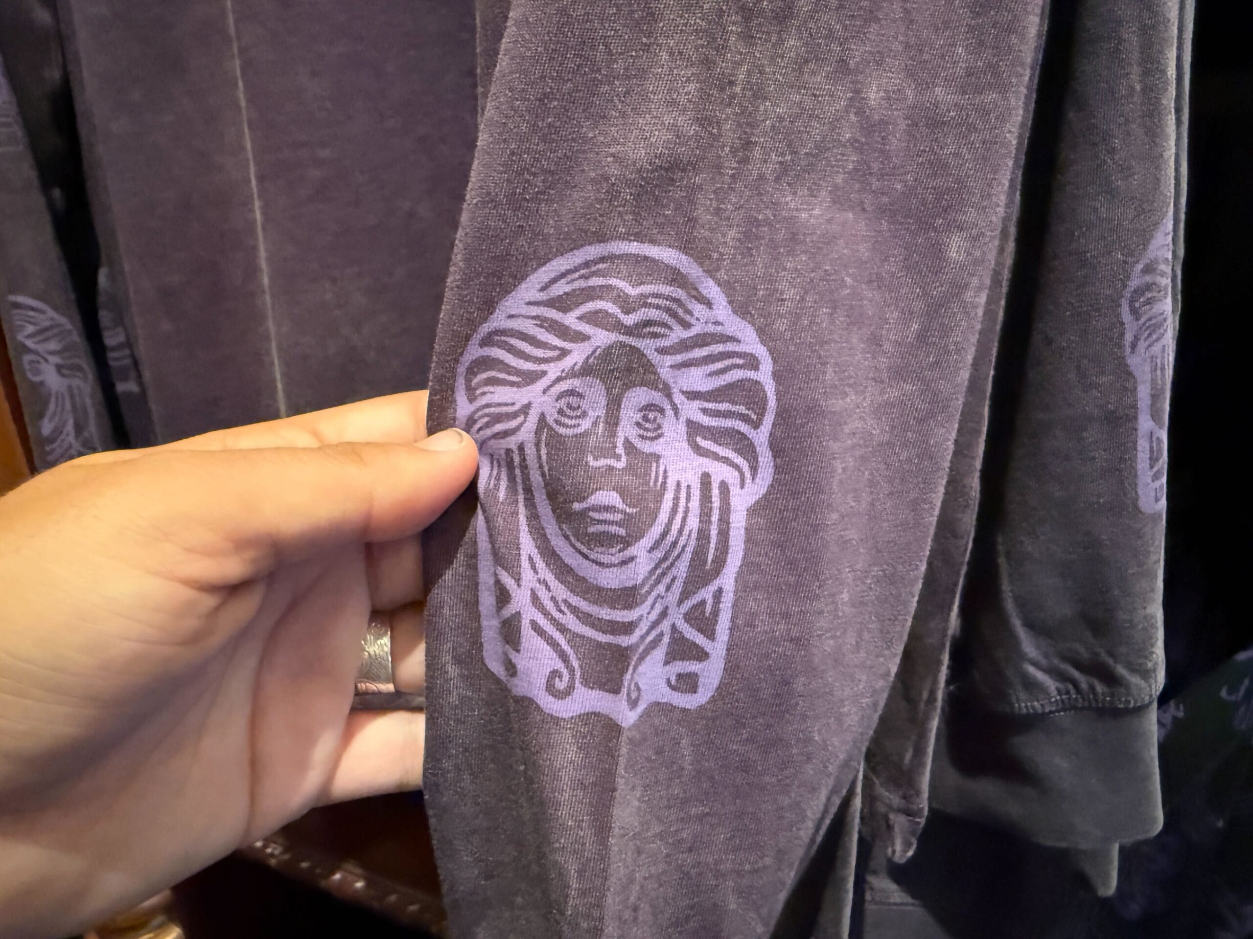 A hand holds a purple fabric sleeve with a Medusa-like face, possibly exclusive HM Merchandise from Disneyland.