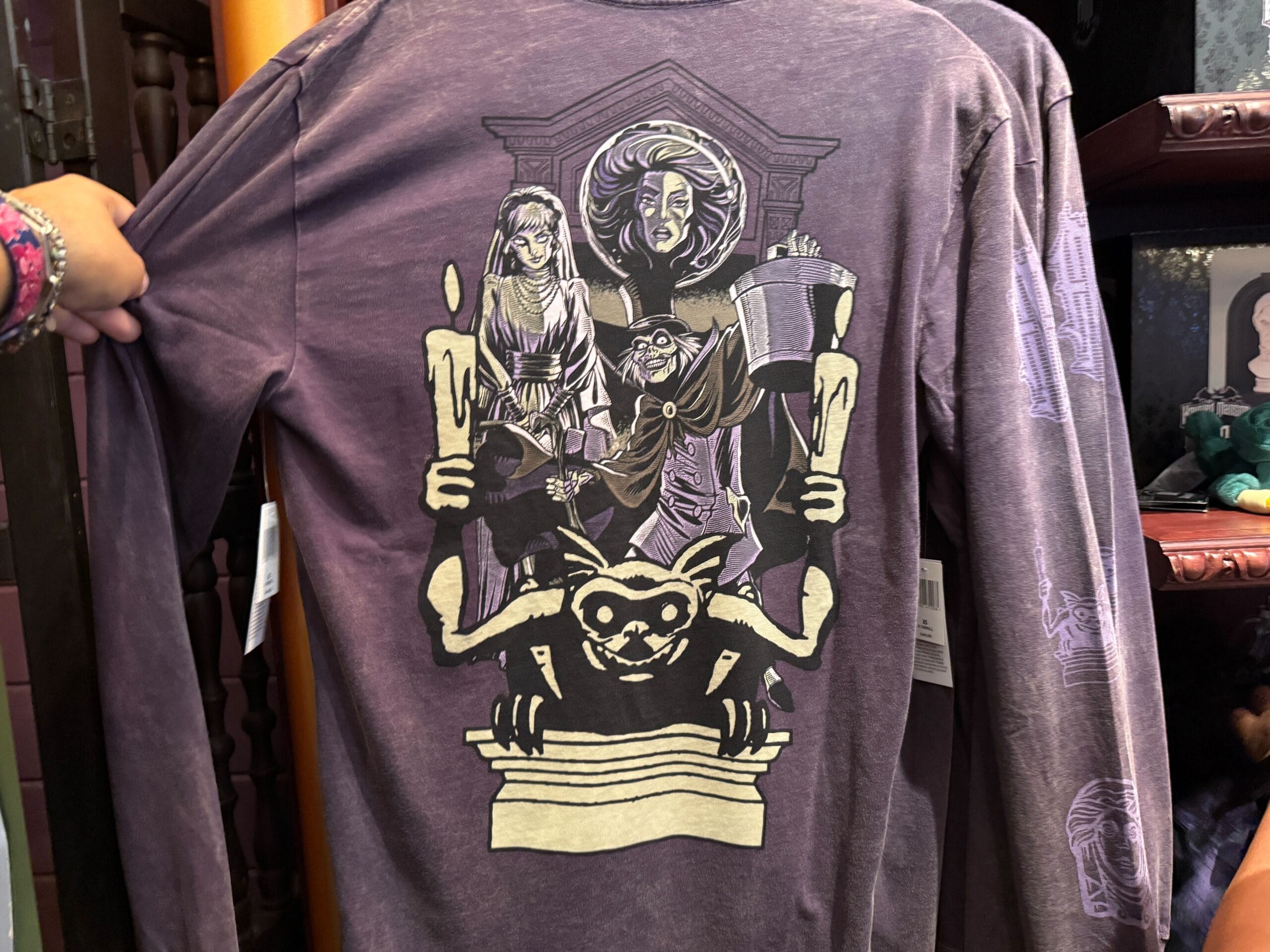 Purple shirt featuring HM Merchandise art: three spooky figures with candles, a bust, and Disneyland's iconic gargoyle below.