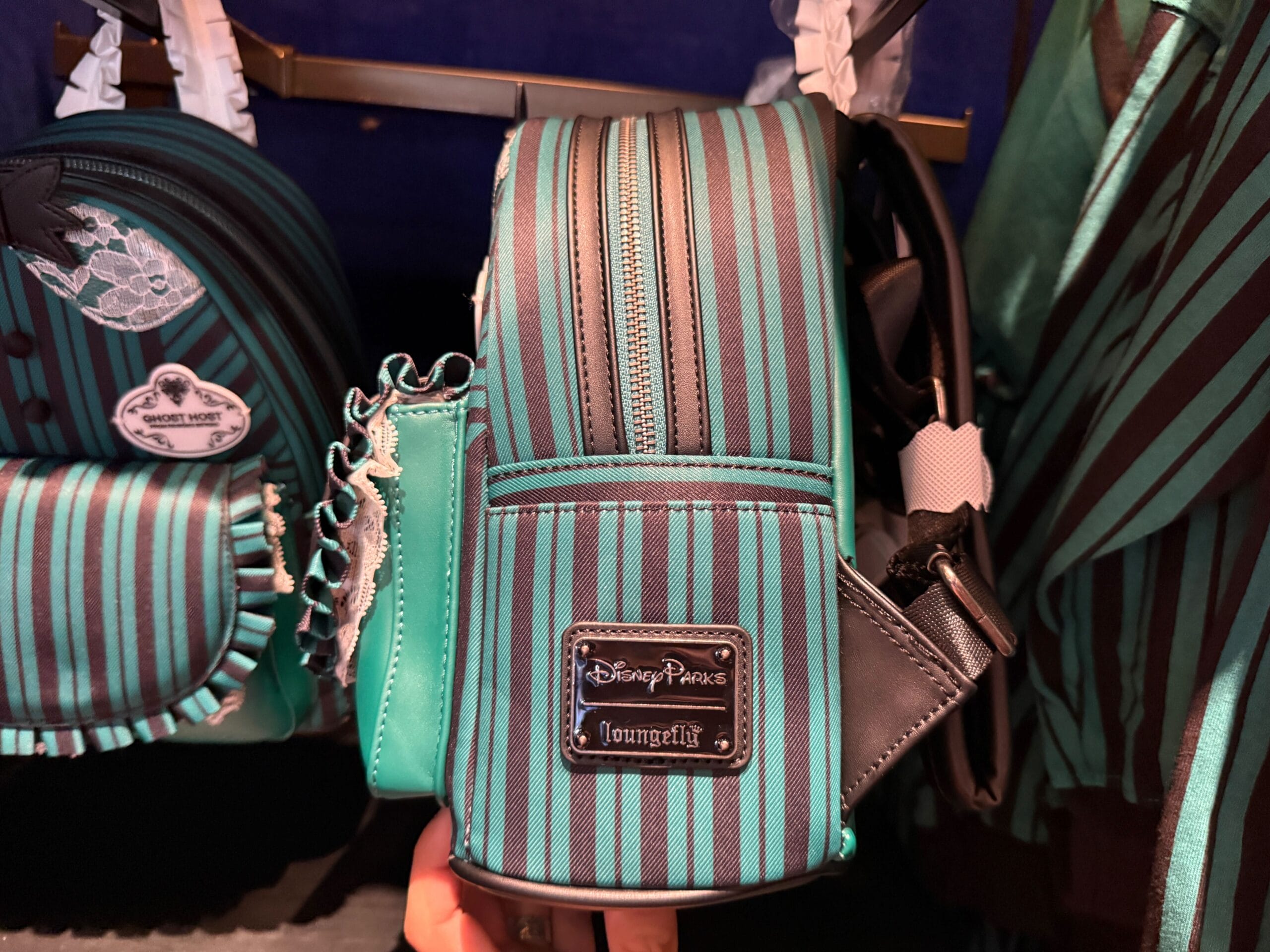 A teal and black striped Disneyland HM Merchandise Loungefly mini backpack hangs on a store display.