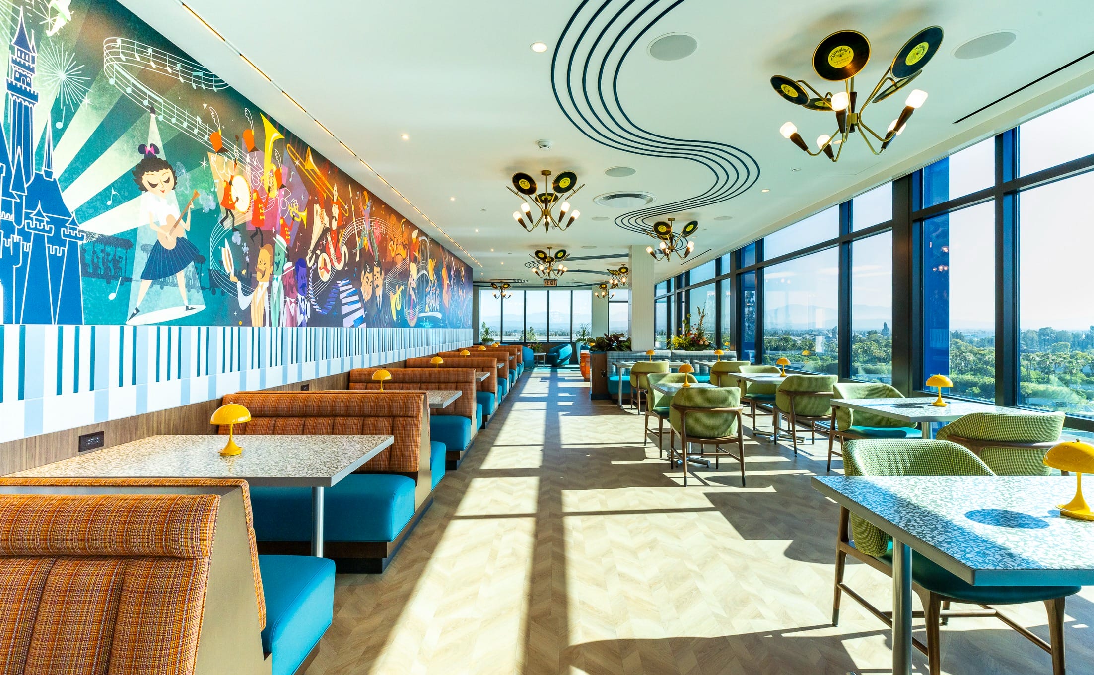 A colorful, retro-style restaurant with booth seating at the Disneyland Hotel, featuring a vibrant mural of dancing figures.