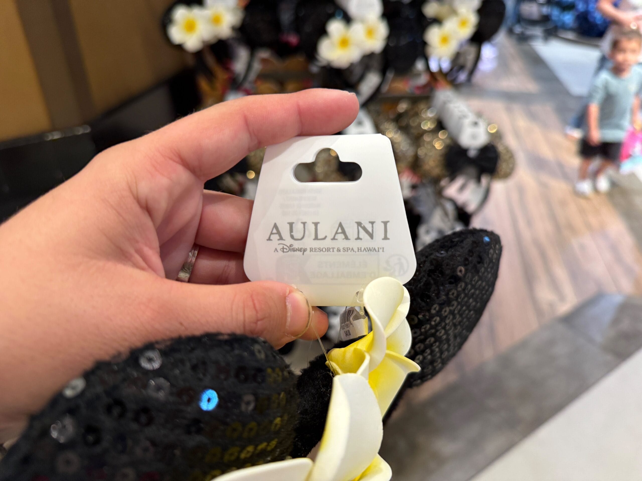 Hand holding a Disney Aulani Resort Minnie Mouse ear headband with black sequins and yellow flower accents.