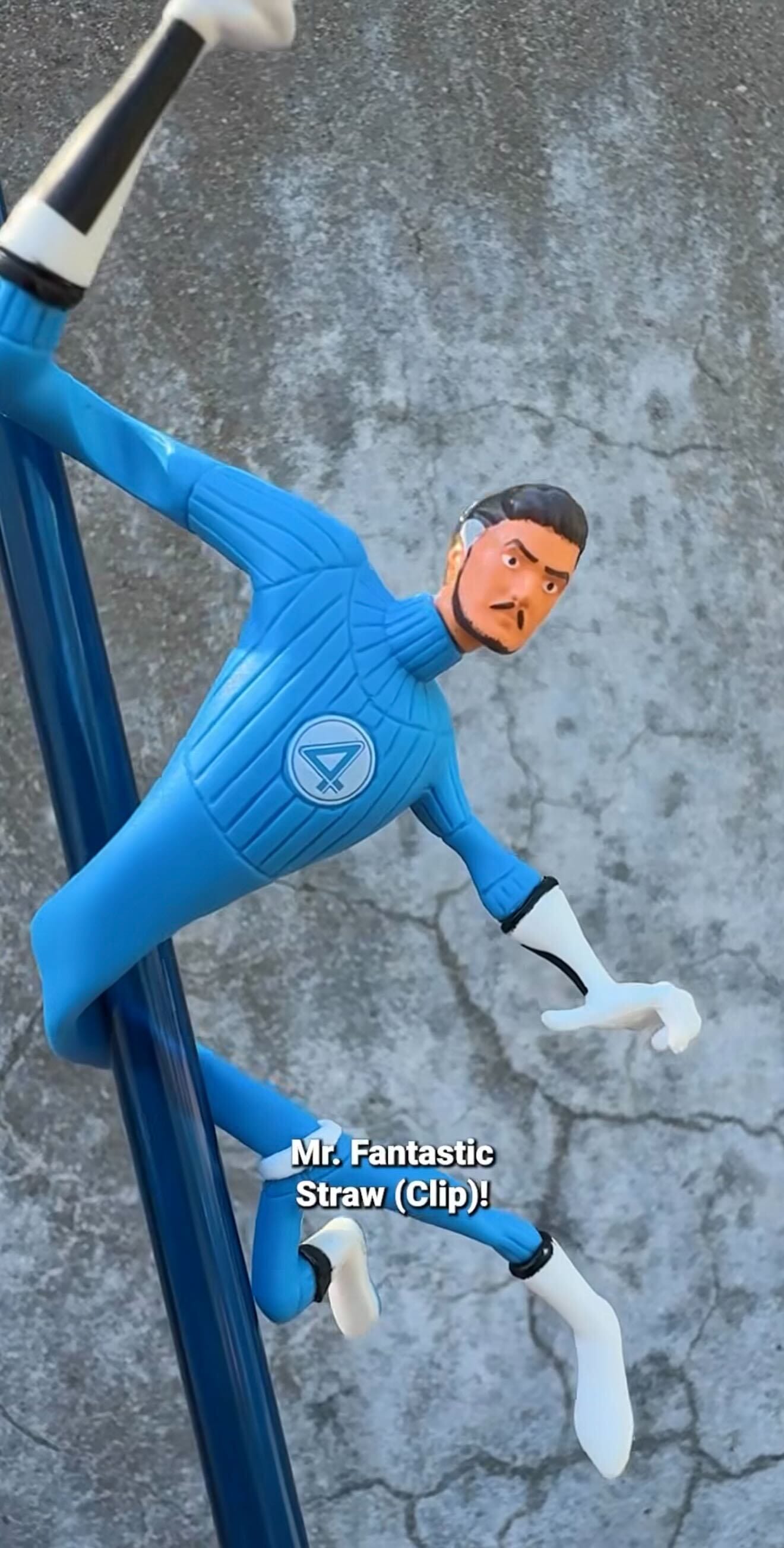A Mr. Fantastic figurine from Fantastic Four is wrapped around a blue straw against a gray textured background.