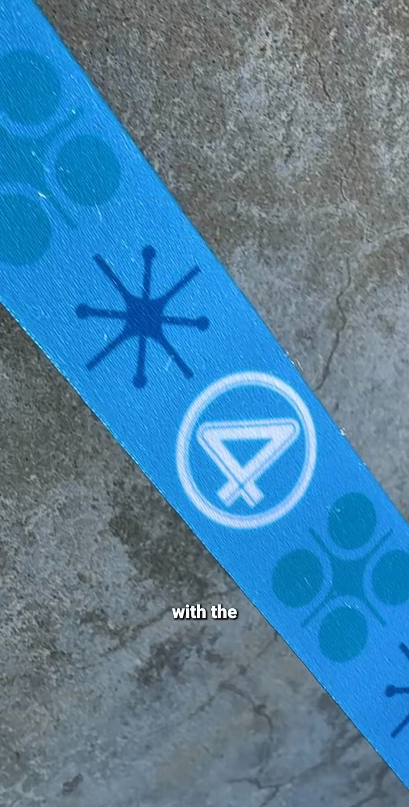A blue strap with a white number 4, reminiscent of Fantastic Four, lies on a rough gray surface with dark blue shapes.