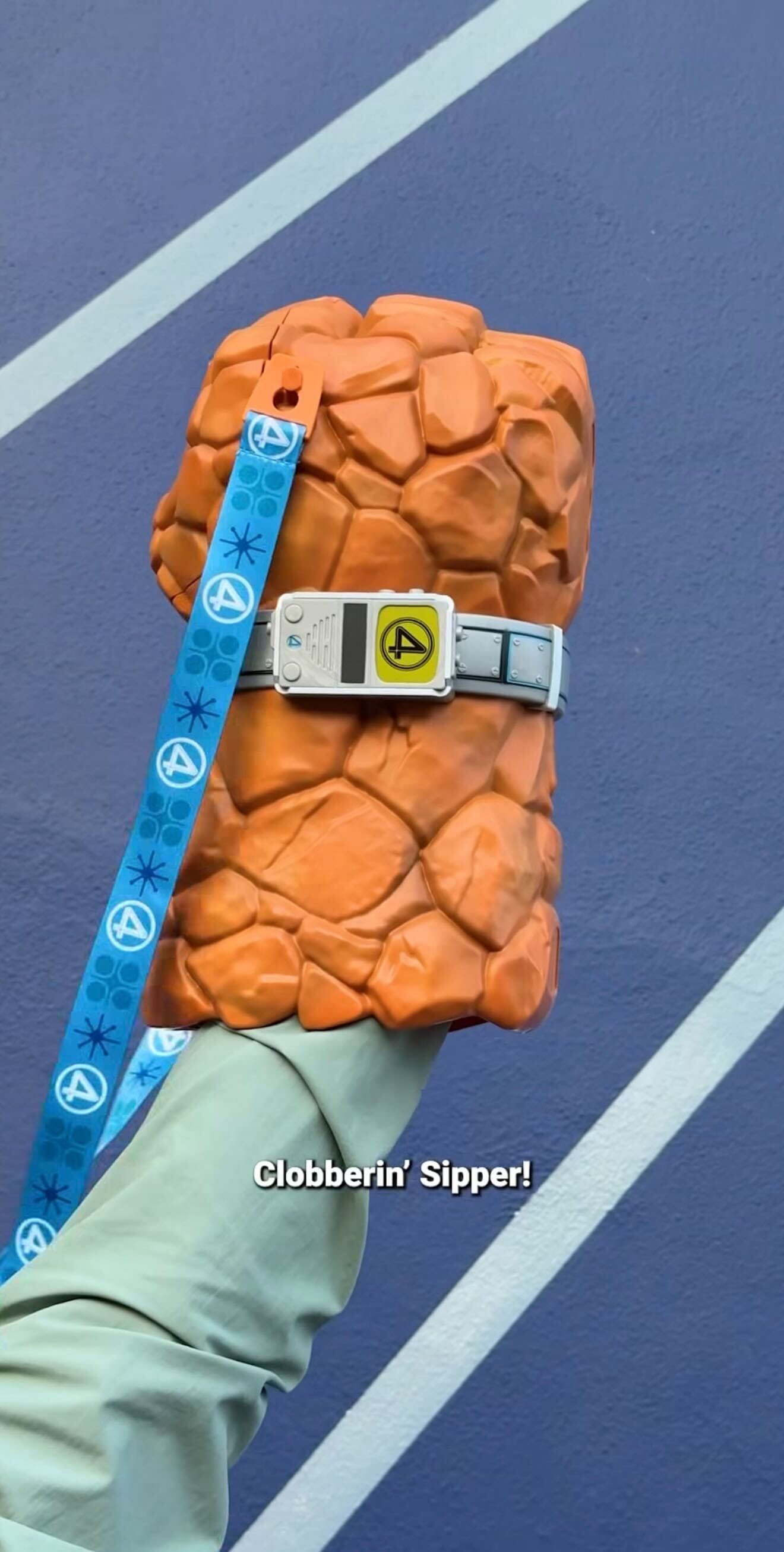 A hand holds a sipper cup shaped like The Thing's rocky fist from Fantastic Four, with a blue lanyard attached.