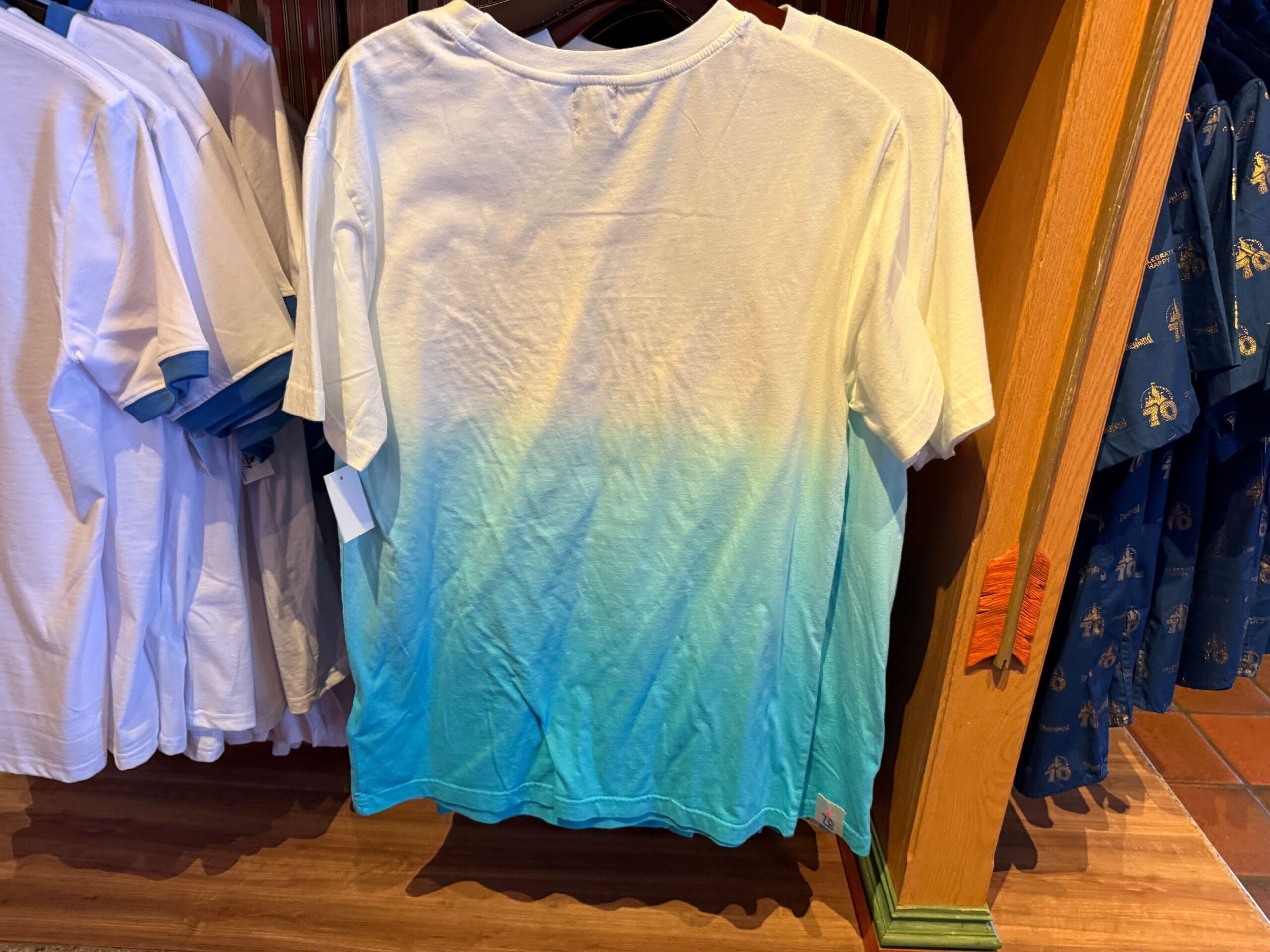 A short-sleeved t-shirt with a white top fading into teal and blue at the bottom, hanging on a store rack.