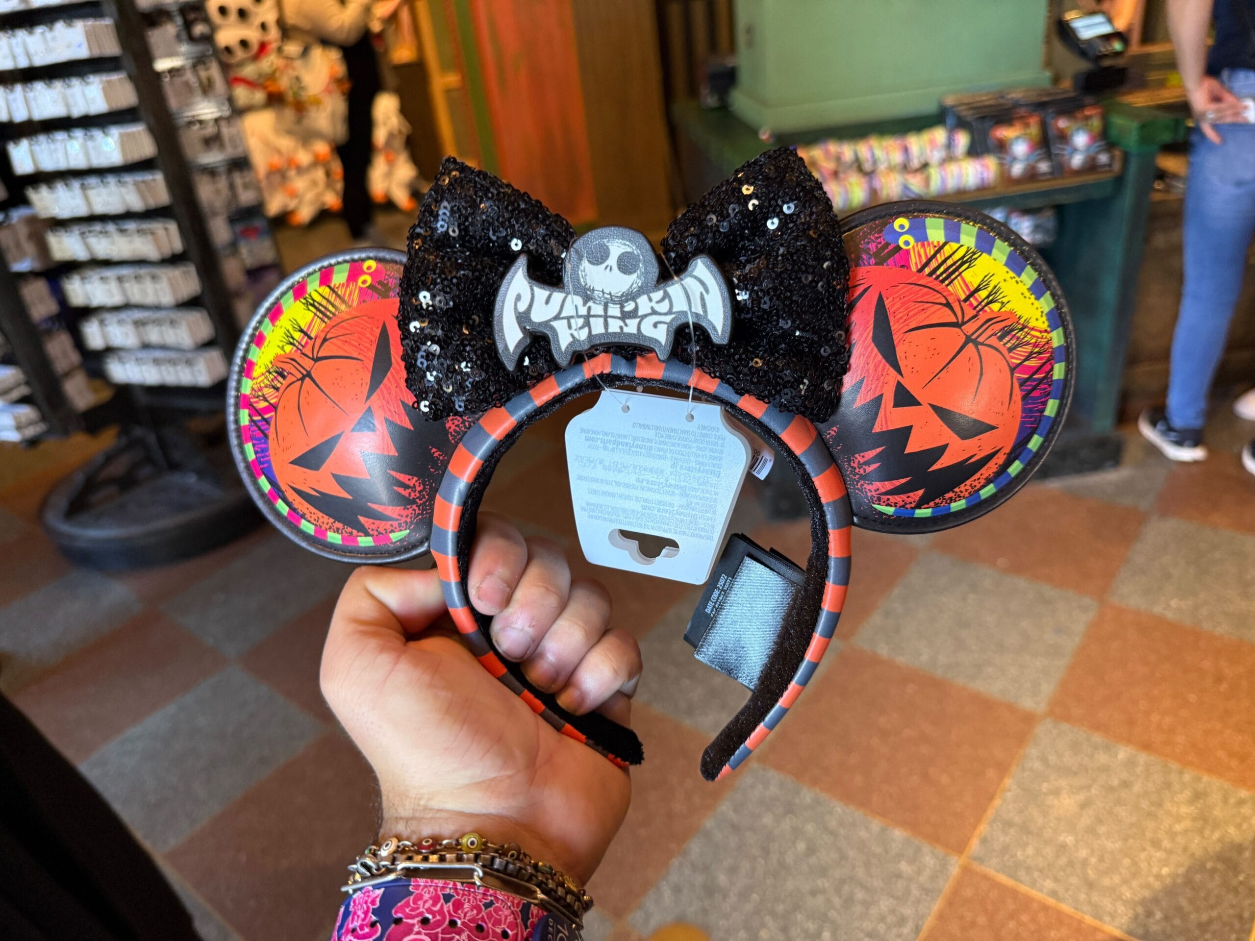 Hand holding Halloween-themed Mickey ears headband with "Pumpkin King" and Jack Skellington design in a store.
