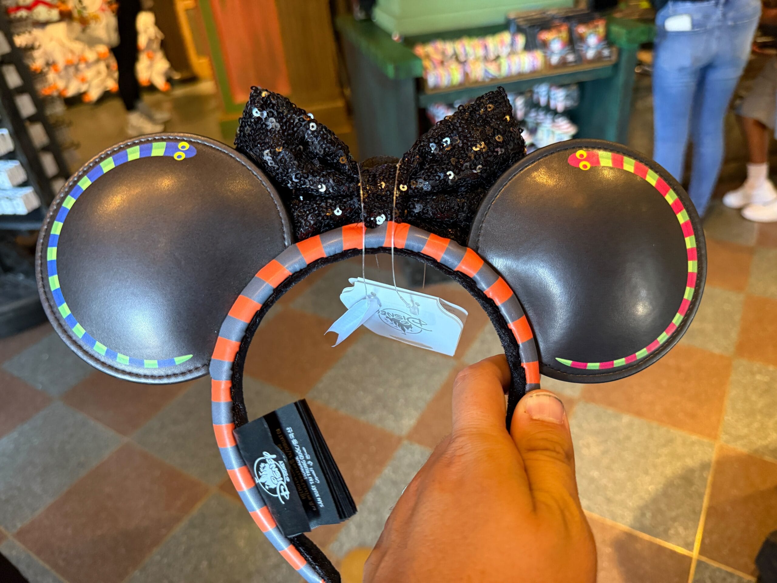 A hand holds a black sequined Minnie Mouse ear headband with Pumpkin King merchandise accents in a store.