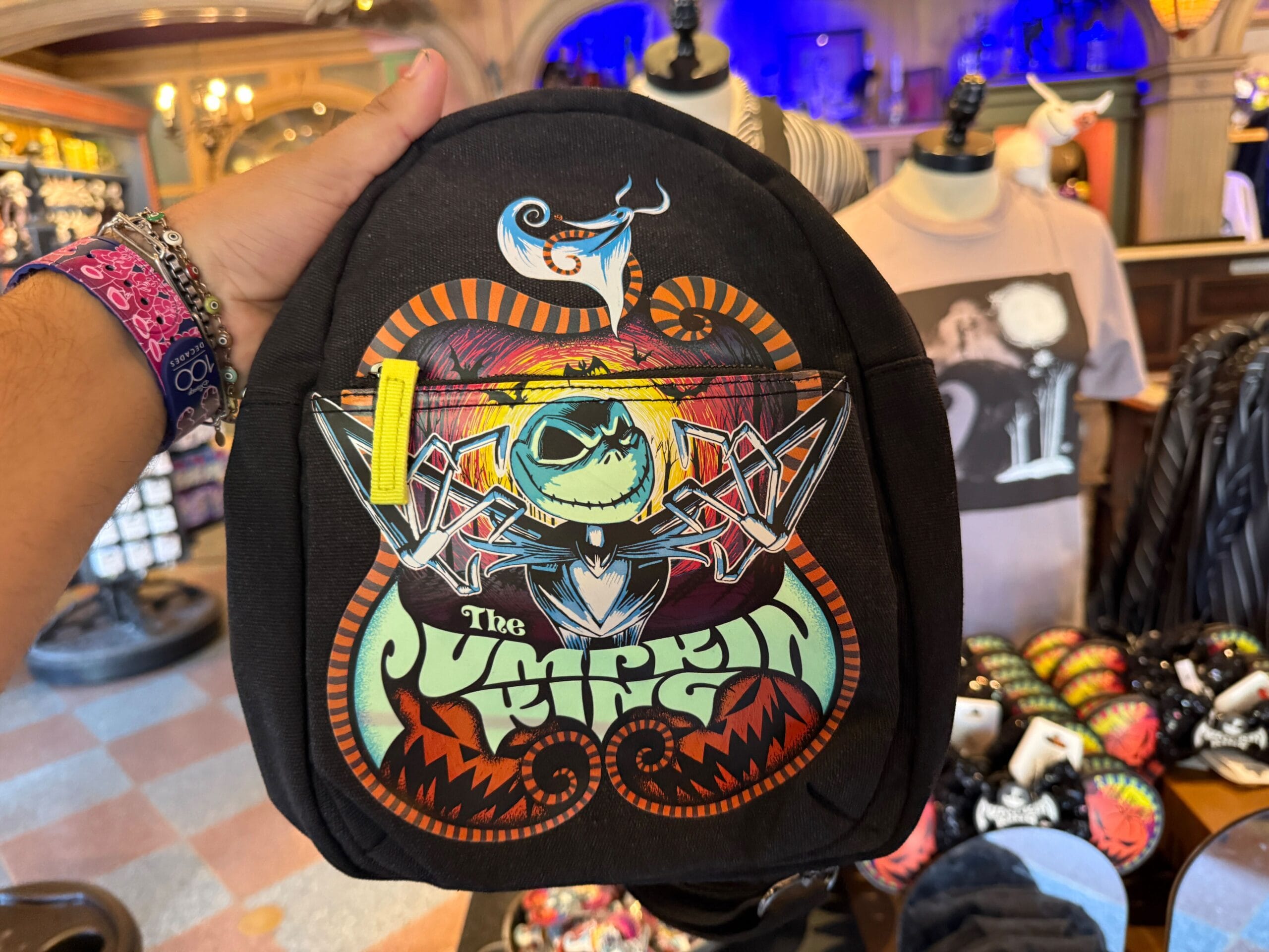 A hand holds a black backpack with colorful art of Jack Skellington and “The Pumpkin King” text.