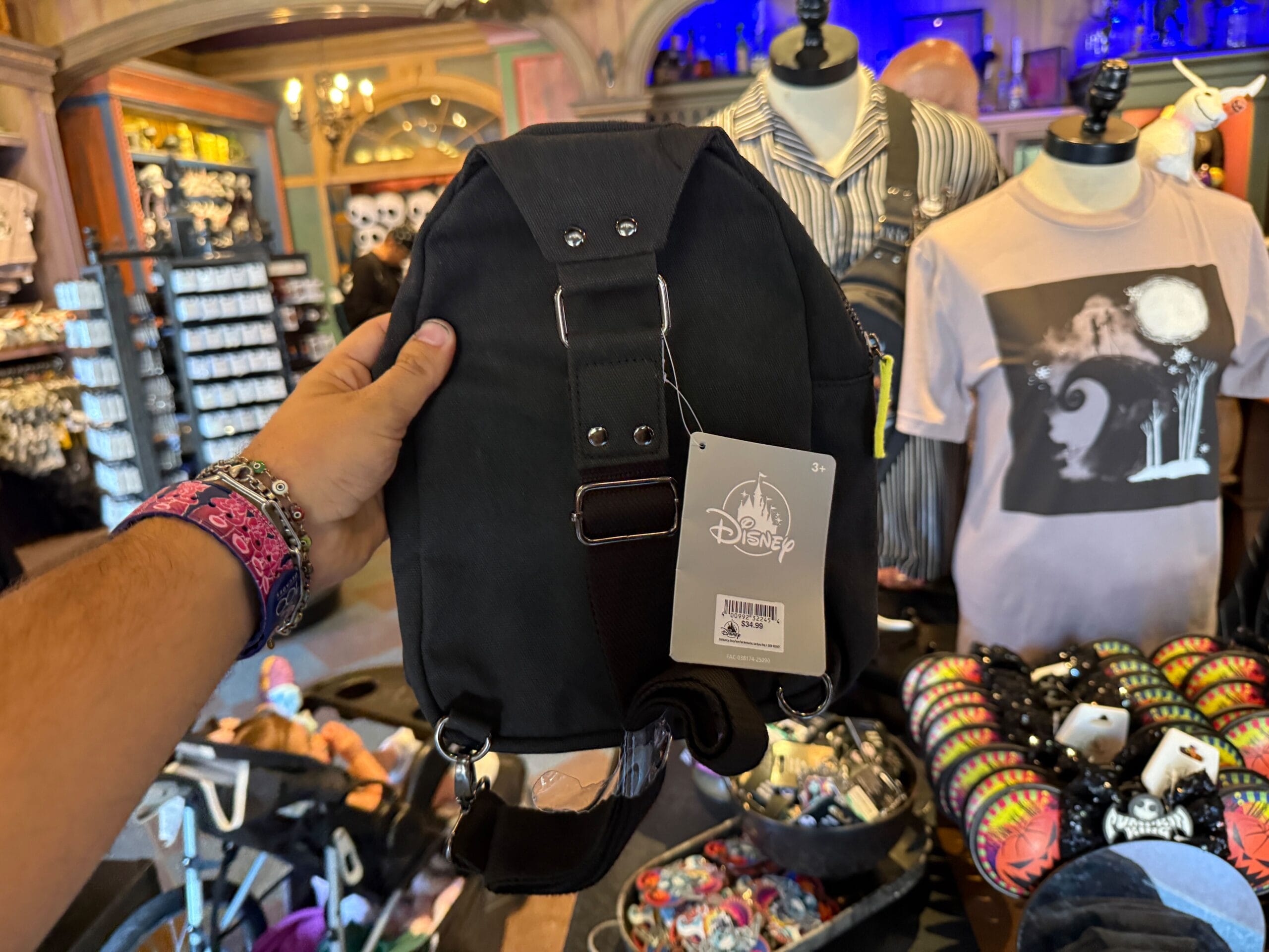 A hand holds a black Disney bag with a tag in a store selling themed shirts and colorful buttons.