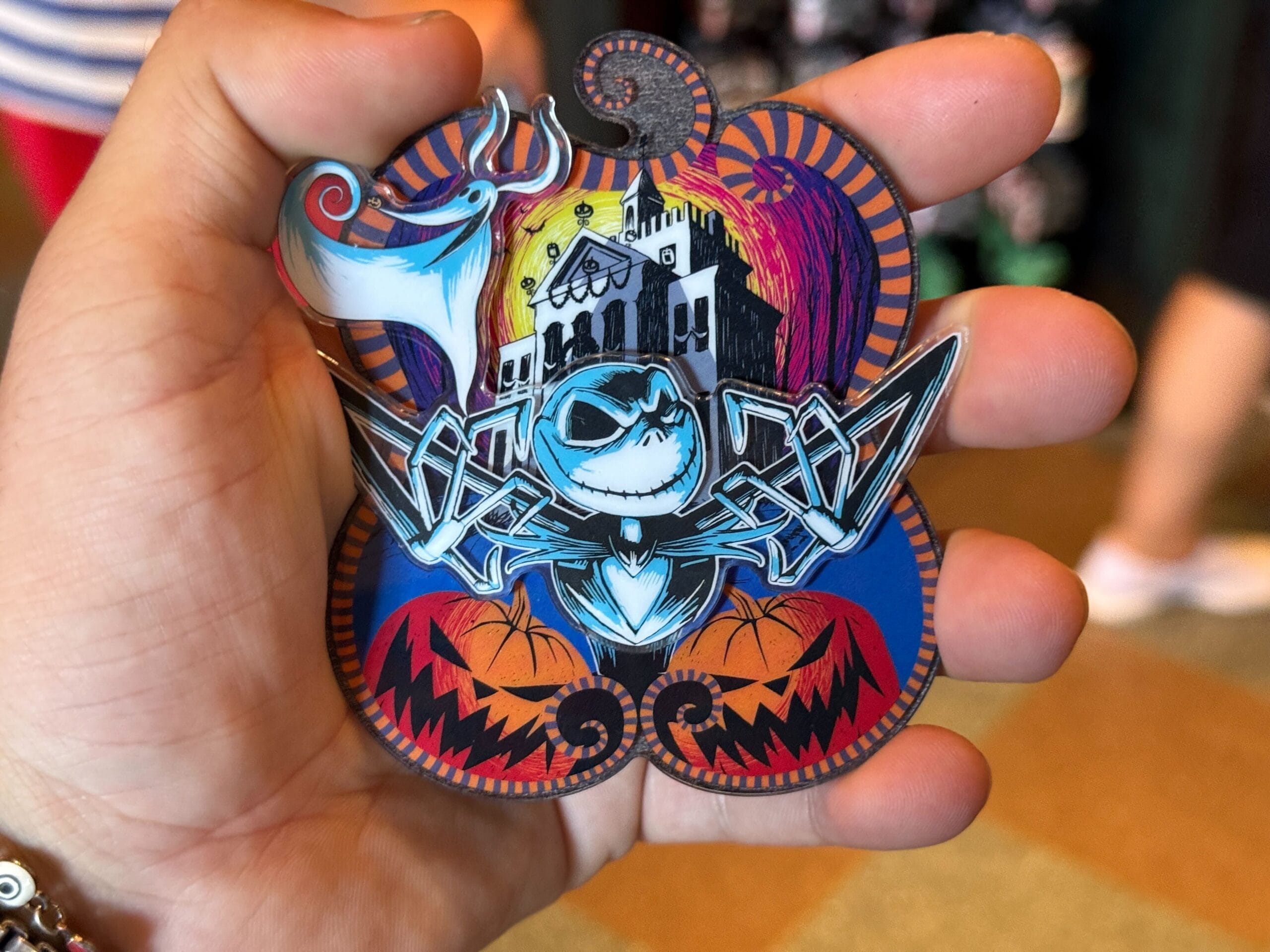 A hand holds a Pumpkin King pin featuring Jack Skellington and Zero from The Nightmare Before Christmas.