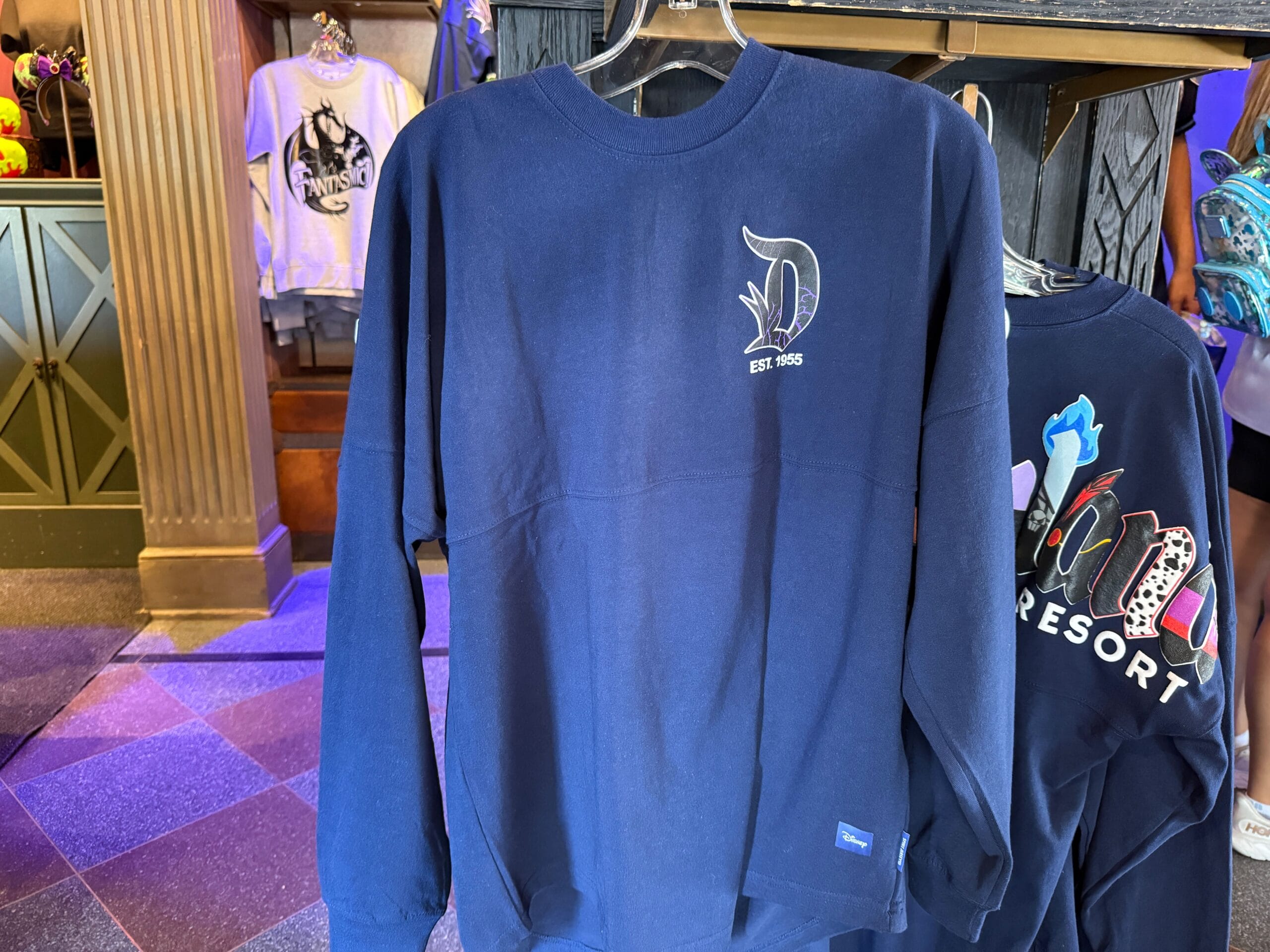 Navy blue long-sleeve shirt with a stylized "D" and "Est. 1955" on display in a store.