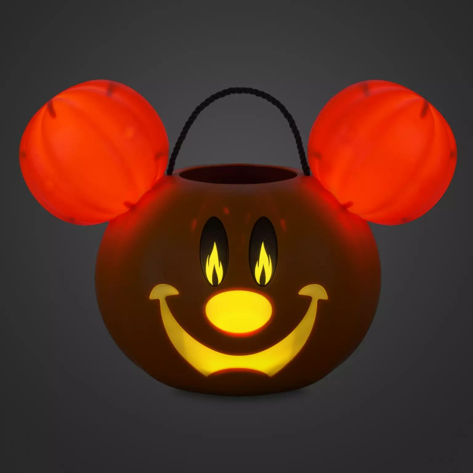 A pumpkin lantern with a glowing Mickey face, part of new Disney Store Halloween merchandise, shines on a dark background.