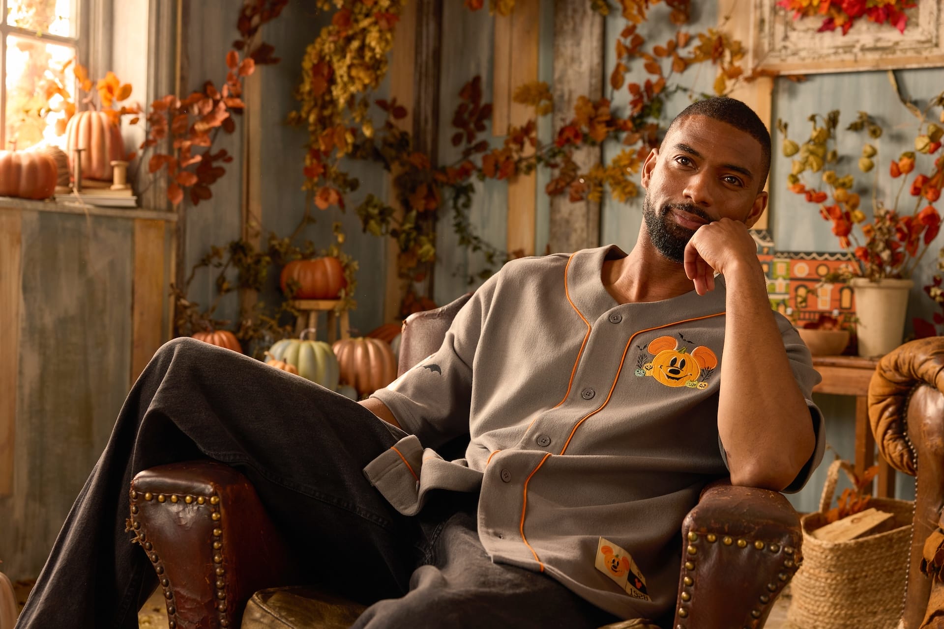 Man in a gray Mickey Mouse shirt sits in a cozy, autumn-themed room with pumpkins from the Disney Store’s Halloween Collection.
