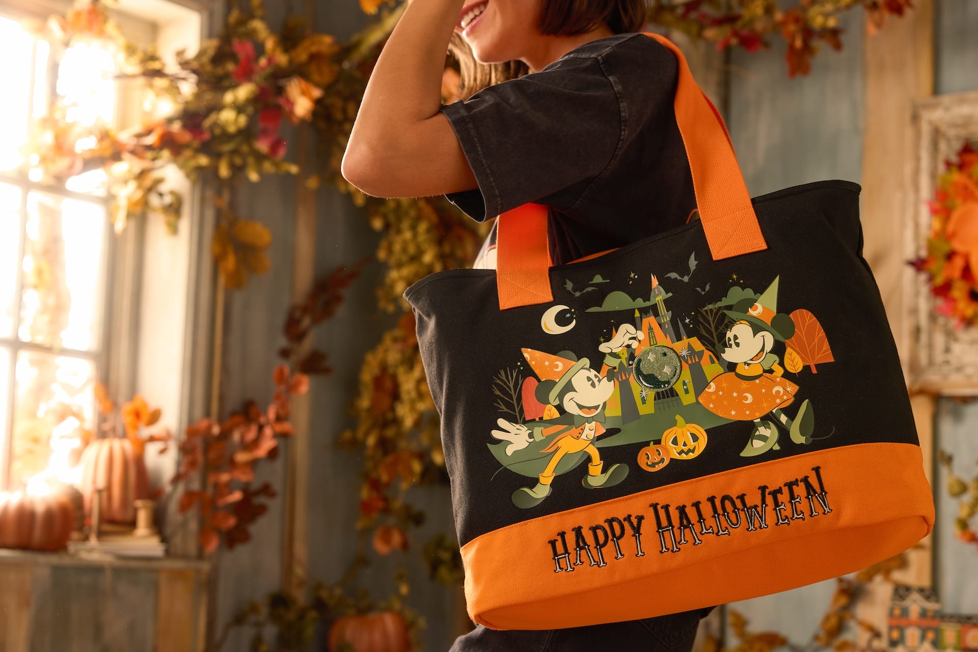 A person holds a Disney Store Halloween Collection tote bag featuring Mickey and Minnie Mouse in costumes with pumpkins.