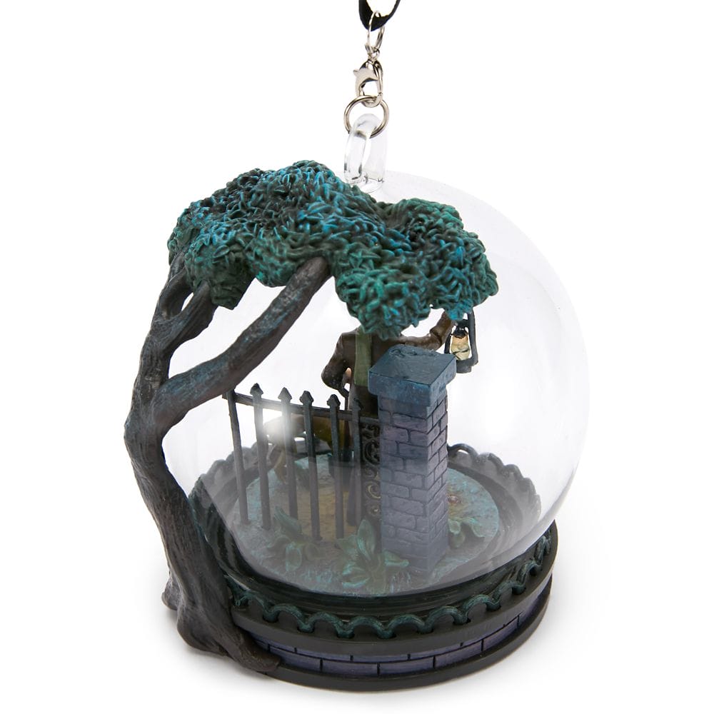 A glass ornament from the Haunted Mansion Collection shows a lantern-bearing figure by a tree and gate.