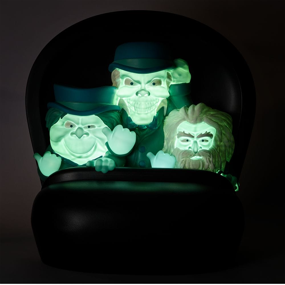 Three glowing green ghosts in suits sit on a dark chair, part of the Disney Store Haunted Mansion Collection.