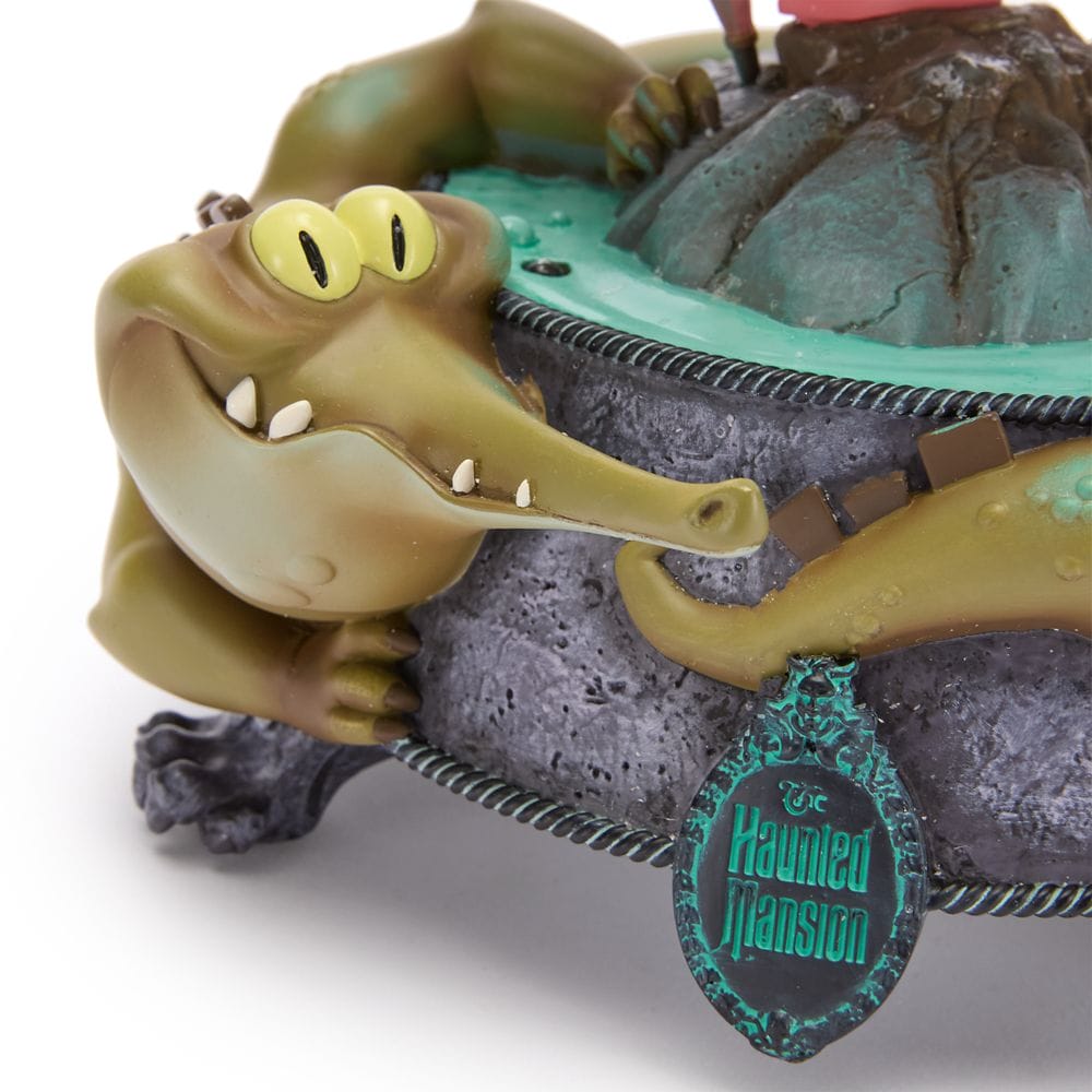 A cartoonish alligator with yellow eyes hugs a stone base labeled "Haunted Mansion" from the Disney Store.